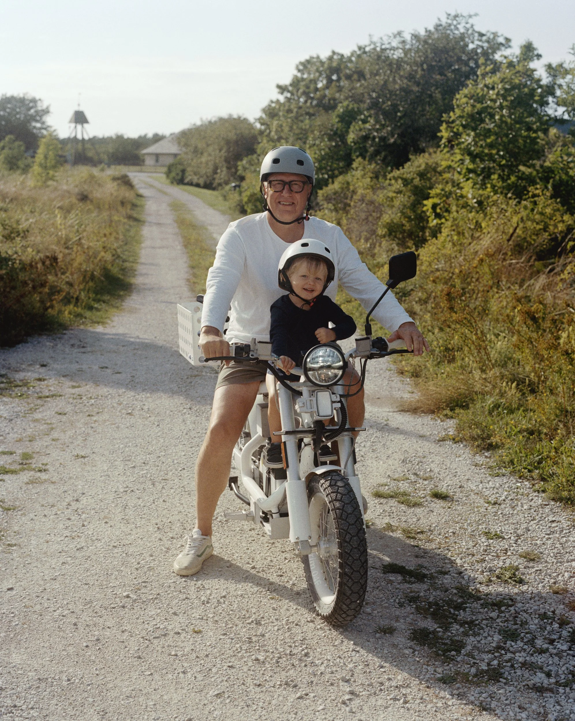 Stefan Ytterborn riding a CAKE motorbike with a young child riding with him. They are stopped on a dirt path, posing and smiling