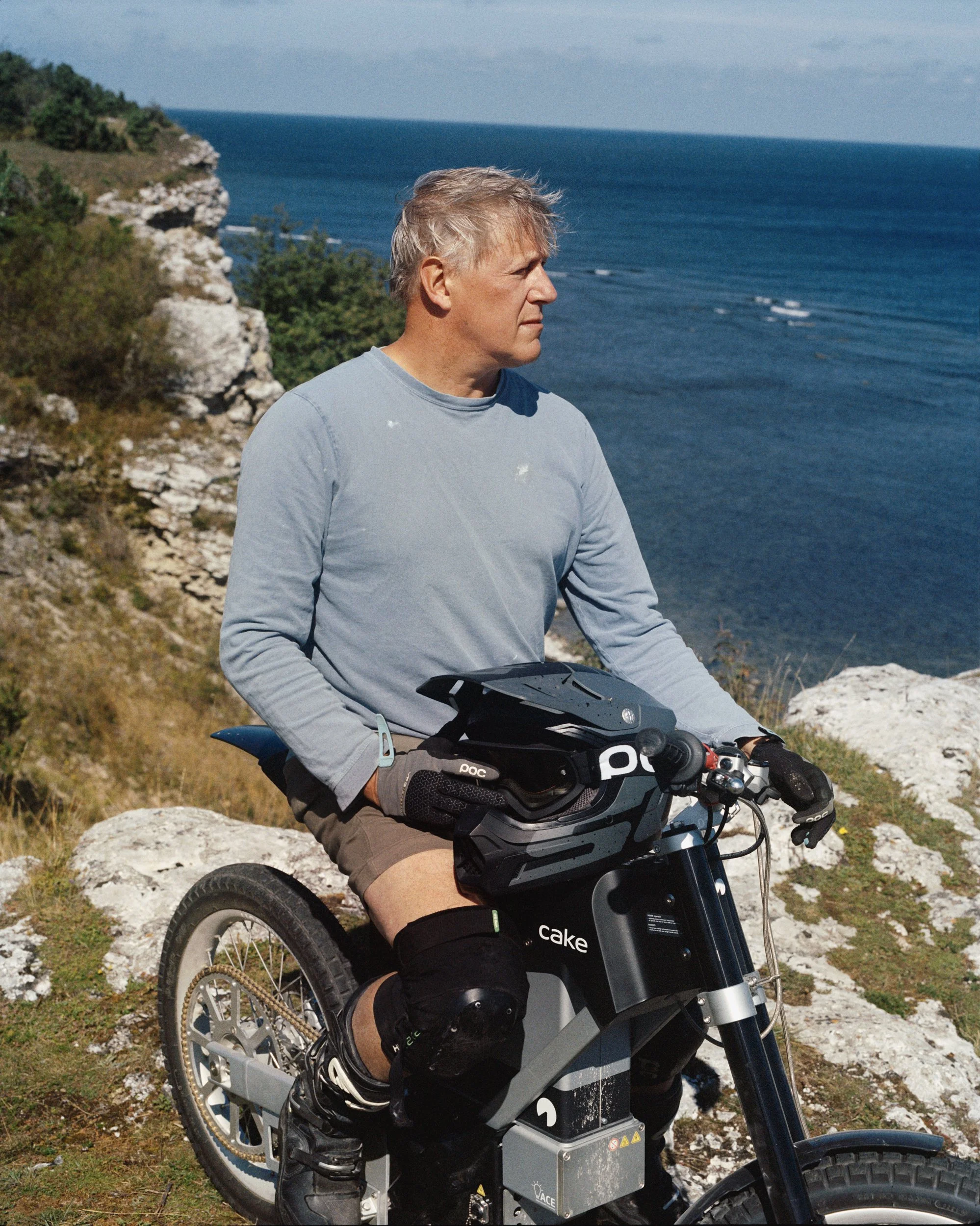 Stefan Ytterborn posing on a CAKE motorcycle overlooking the sea. He has taken his helmet off and is looking out on the water