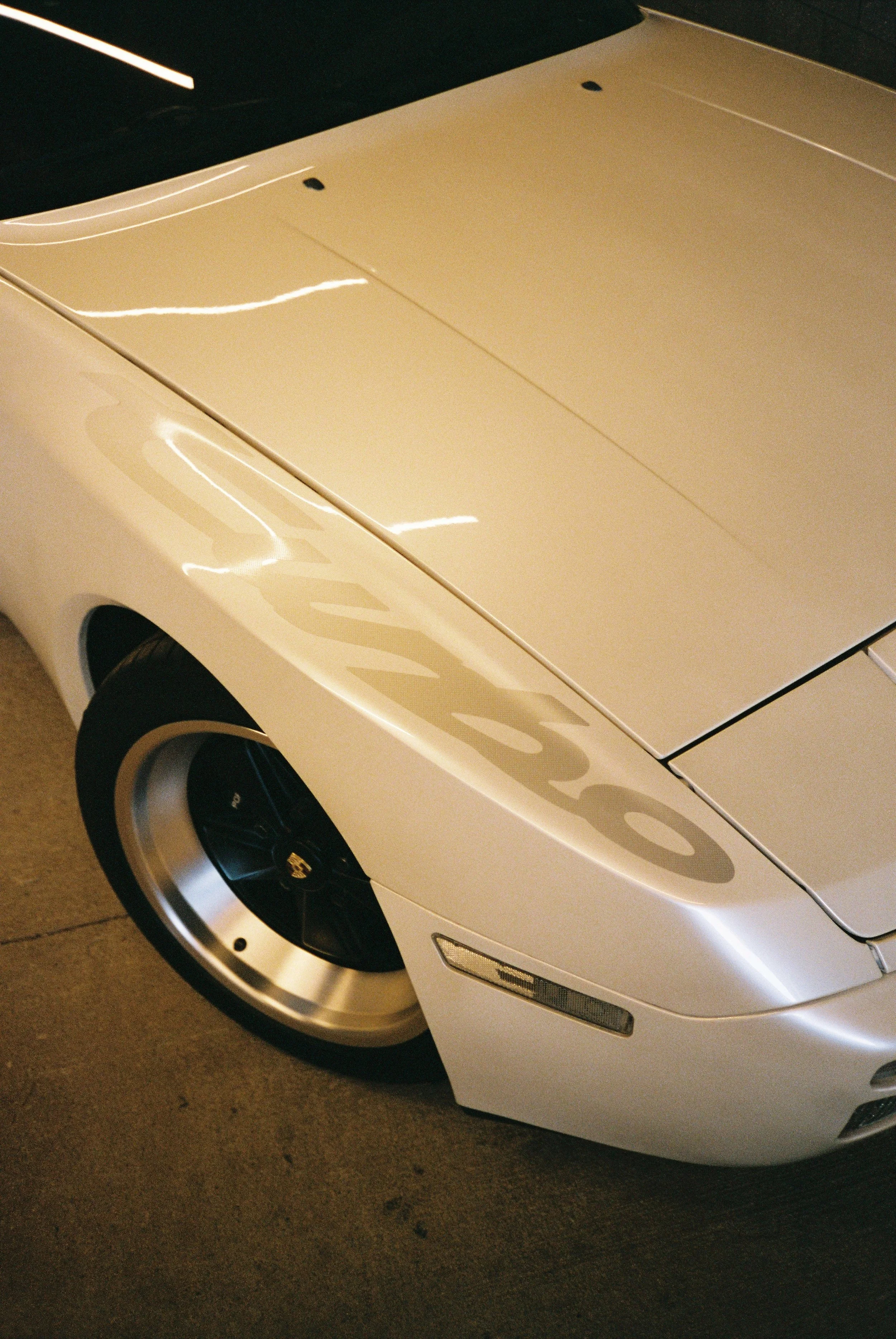 A film photography closeup detail of a wheel and front decal reading "Turbo" on one of the cars on display at the event
