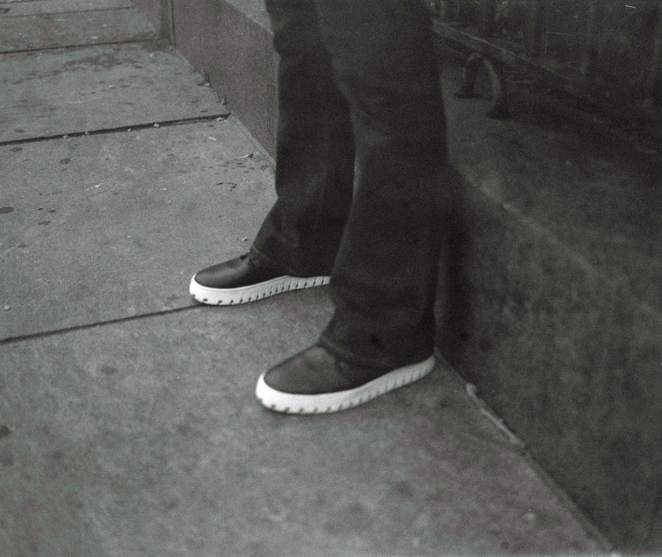 A closeup of someone standing on the street in IAMBIC shoes