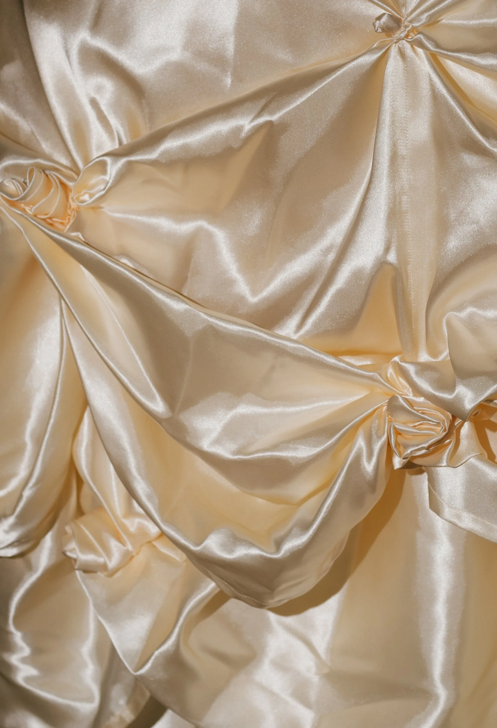 Close-up of cream-colored, shiny satin fabric with gathered and twisted sections.