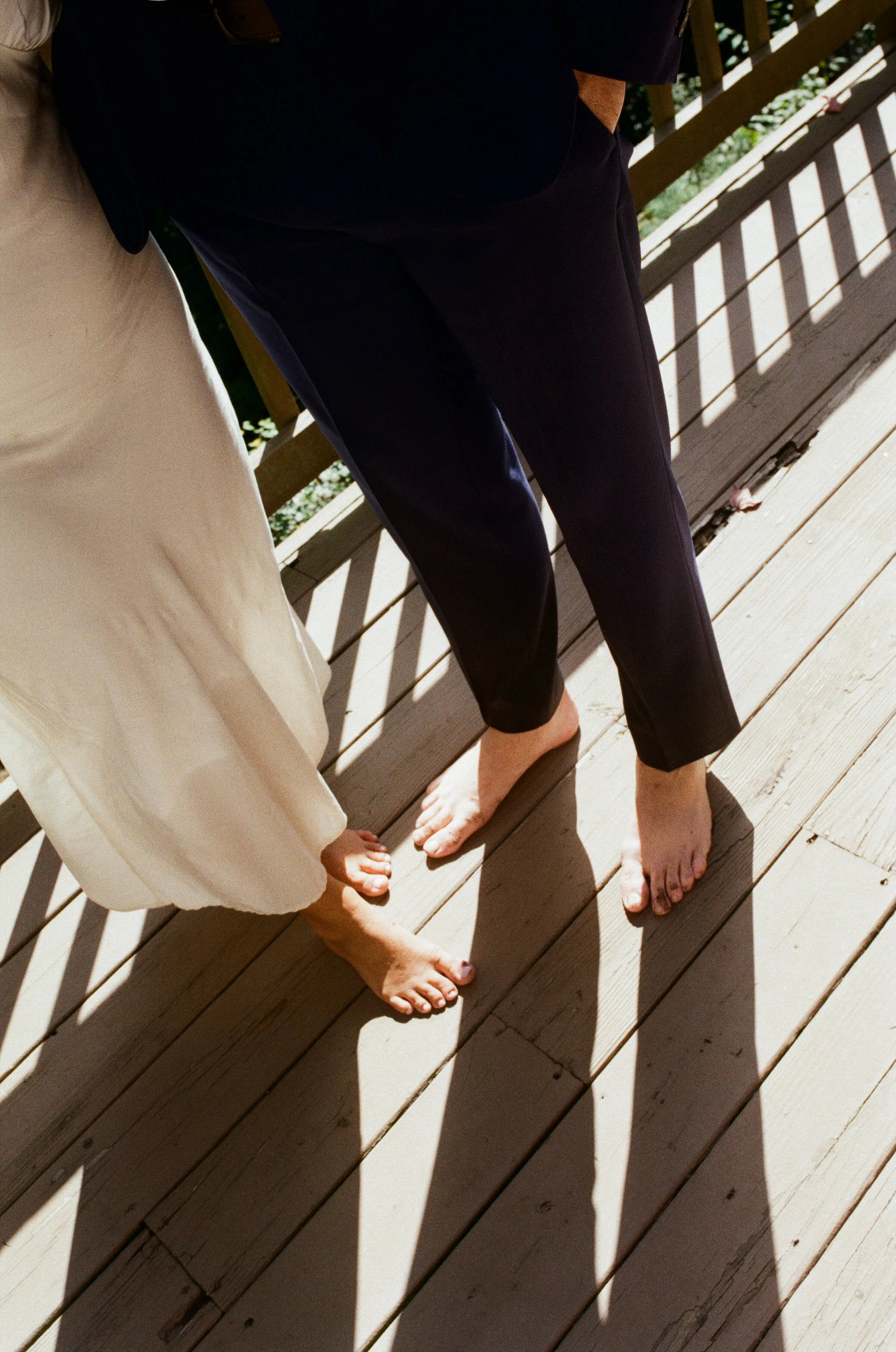 Bare feet of two people standing on a wooden porch with sunlight and shadows.