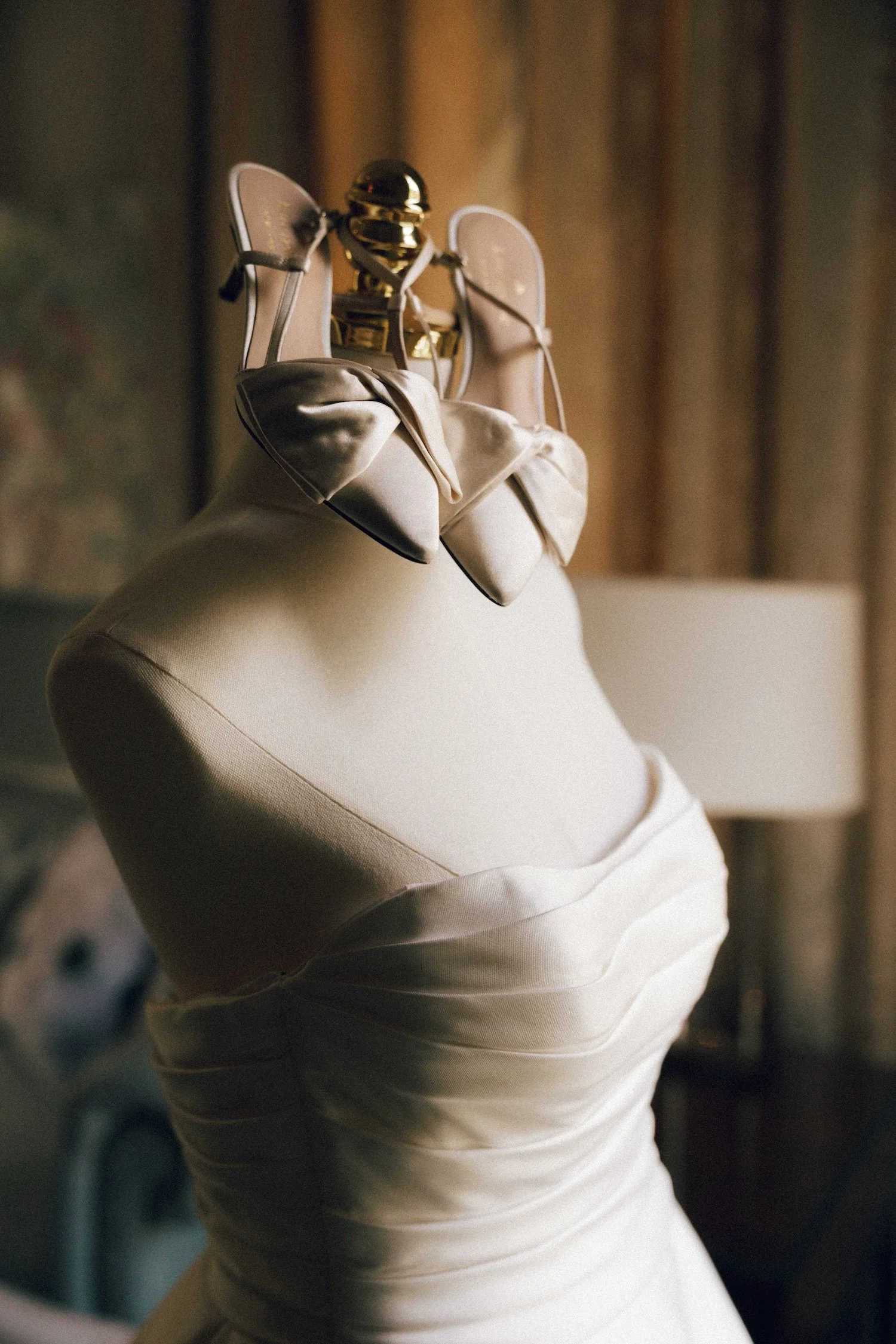 A wedding dress displayed on a mannequin with a pair of beige satin shoes with bows and a gold shoe stretcher.