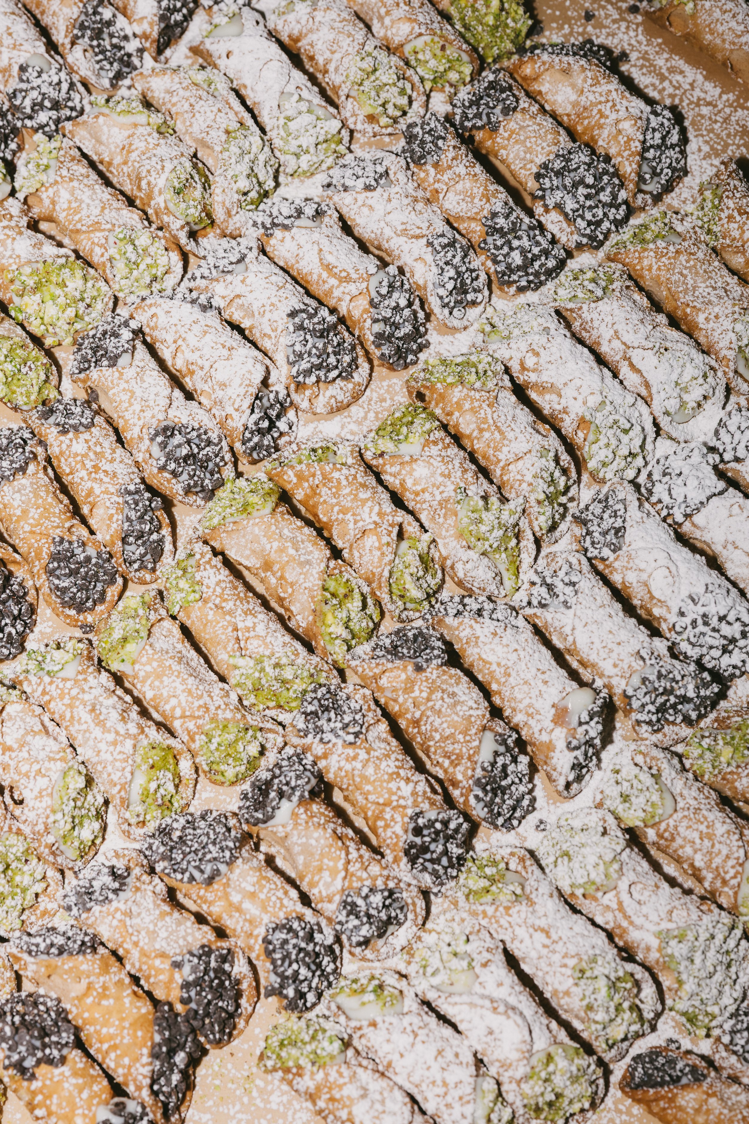 Assorted cannoli pastries sprinkled with powdered sugar, filled with cream and topped with blackberries and pistachios.