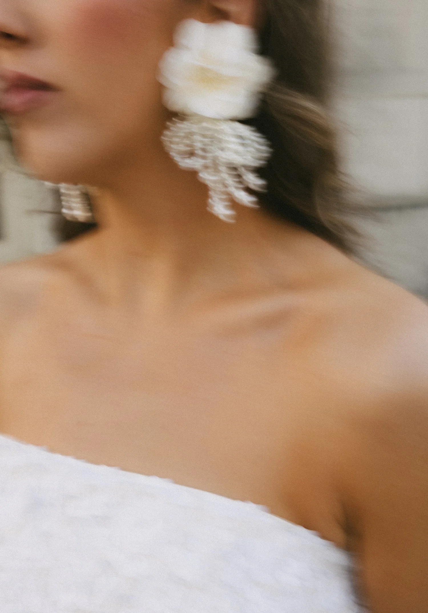 Close-up of a woman with large white floral earrings and wearing a white strapless top