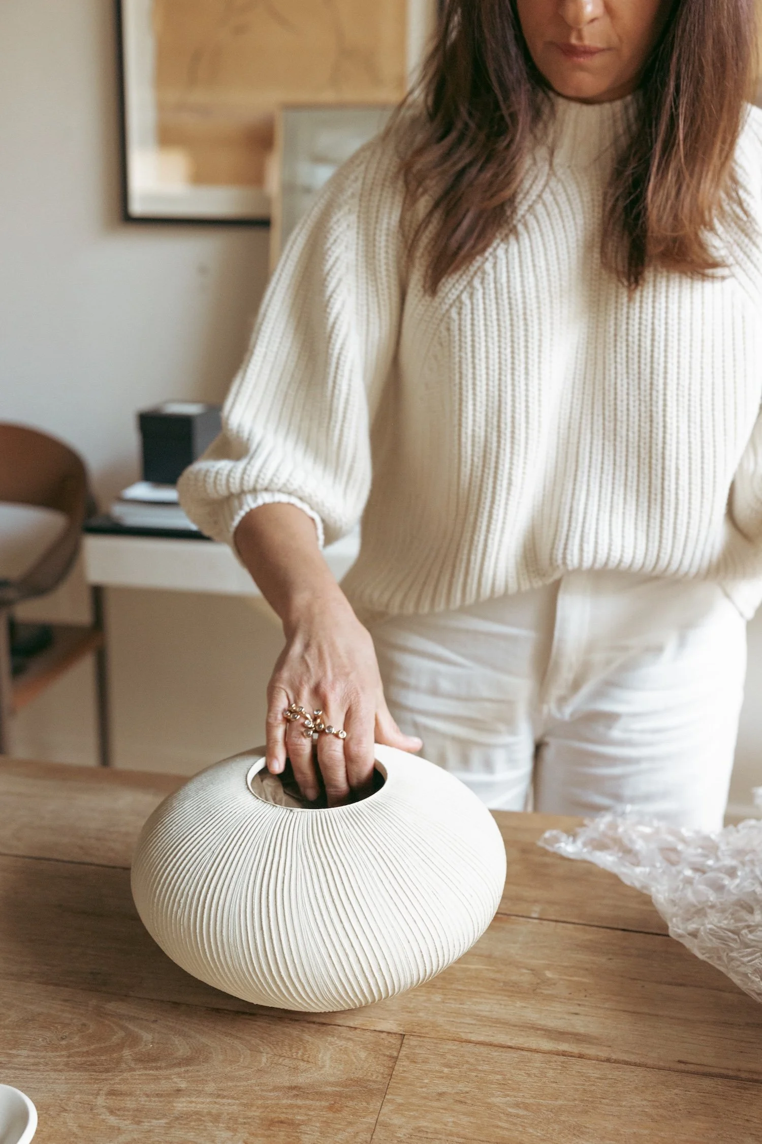 A woman placing her hand into a textured white ceramic vase on a wooden table.