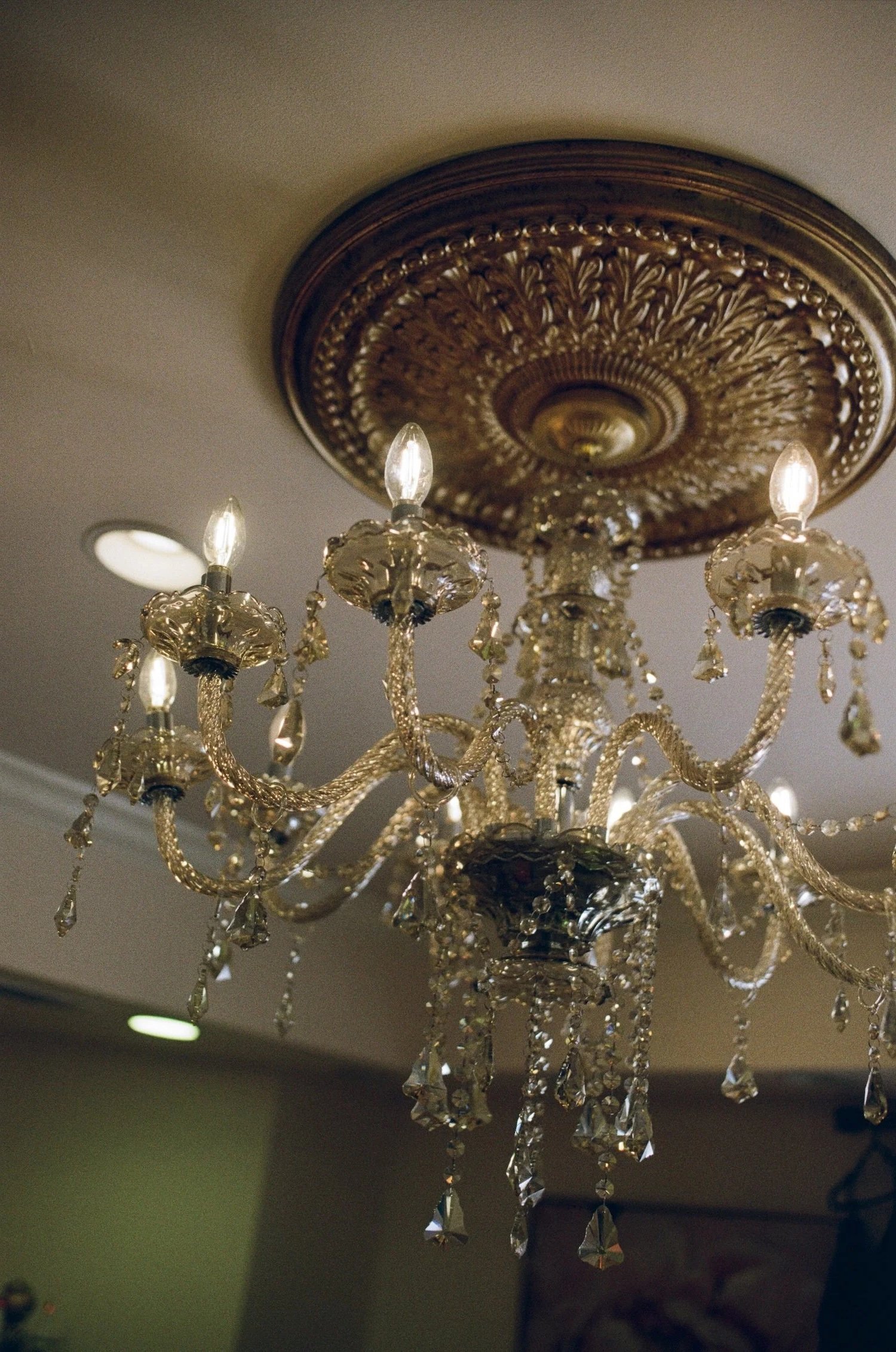 A decorative chandelier with multiple crystal drops hangs from a ceiling medallion, with several small light bulbs illuminating the fixture.