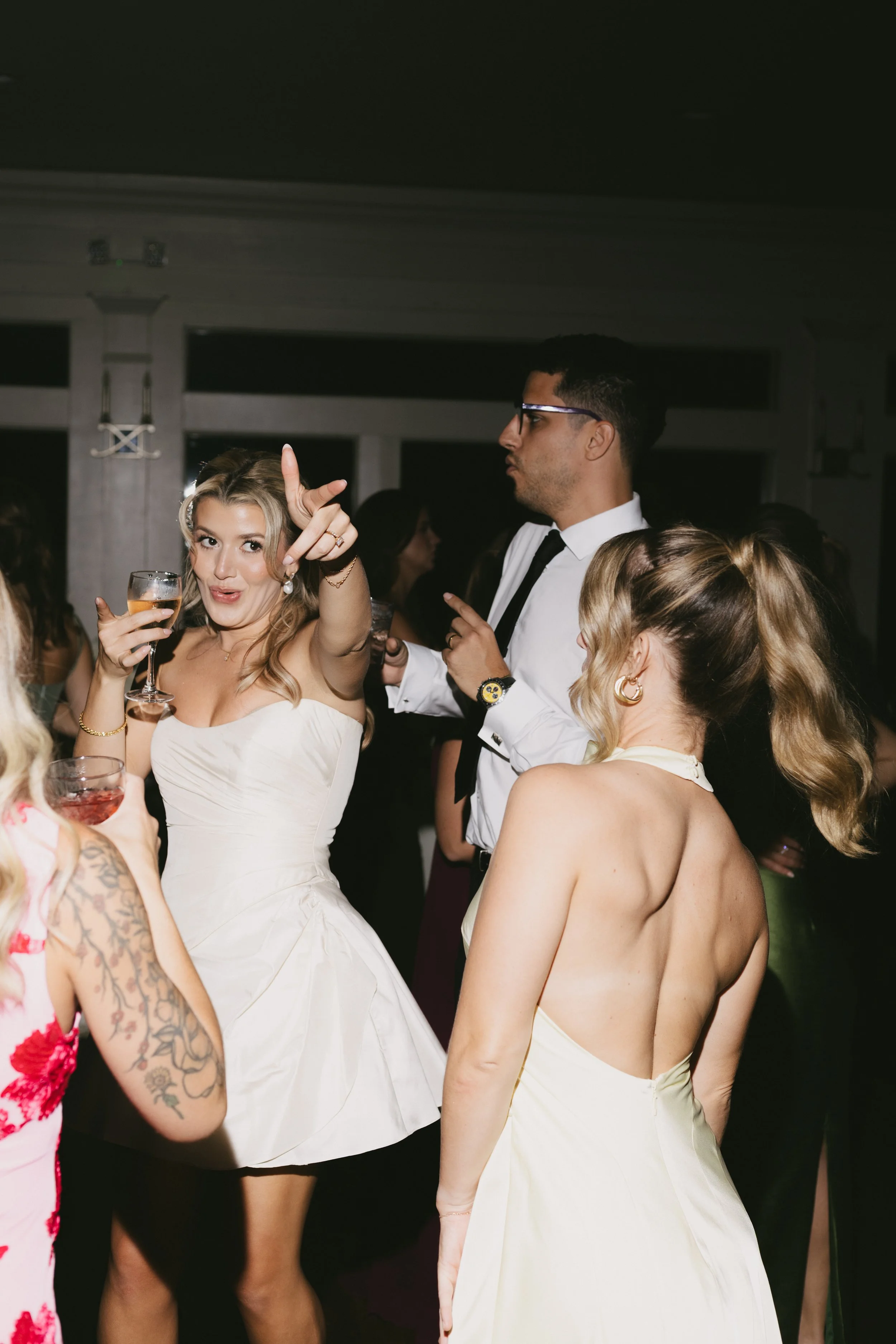 People dancing and socializing at a party, with women in elegant dresses and a man in a white shirt and tie.