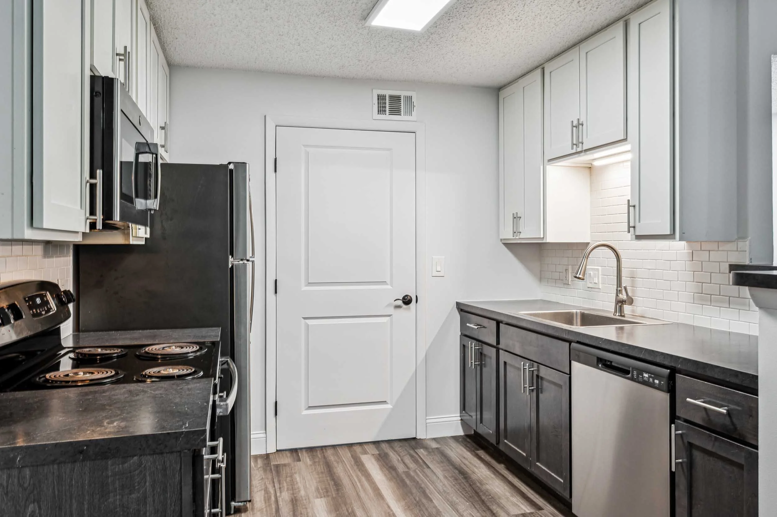 Modern kitchen with white cabinets, black countertop, stainless steel appliances, and wooden floor.