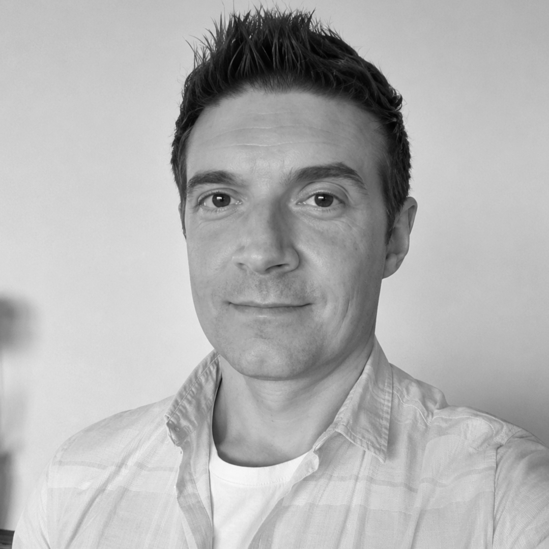 Black and white portrait of a man with short dark hair, wearing a collared shirt, smiling slightly, against a plain background.