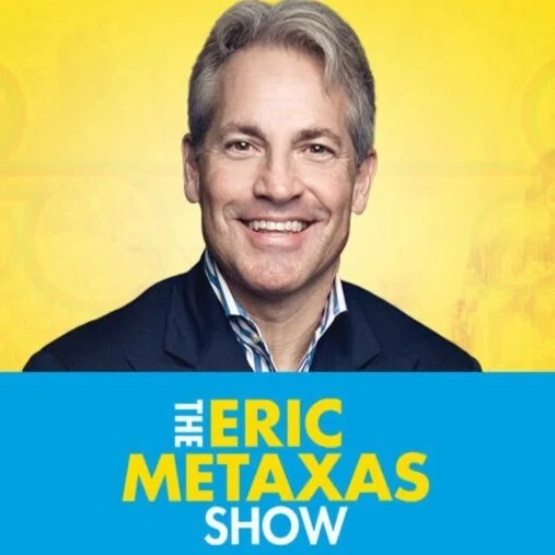 Portrait of Eric Metaxas smiling against a yellow background, with a blue overlay at the bottom displaying his name and show title.