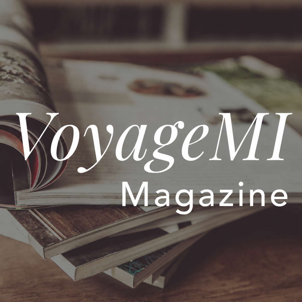 Cover of VoyageMI Magazine featuring an open magazine with pages curled, placed on a wooden surface.