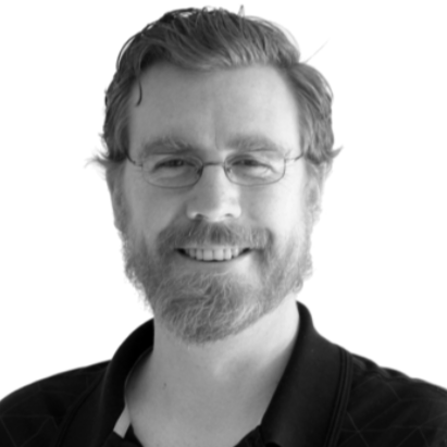 Black and white portrait of a man with glasses, a beard, and short hair, smiling at the camera.