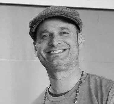 Black and white photo of a smiling man wearing a newsboy cap and a casual shirt.