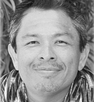 Close-up black-and-white portrait of a smiling man with short hair and a patterned shirt.