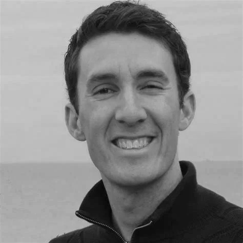 A young man smiling outdoors in black and white.
