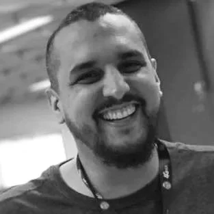 Black and white photo of a smiling man with short hair and a beard, wearing a lanyard.
