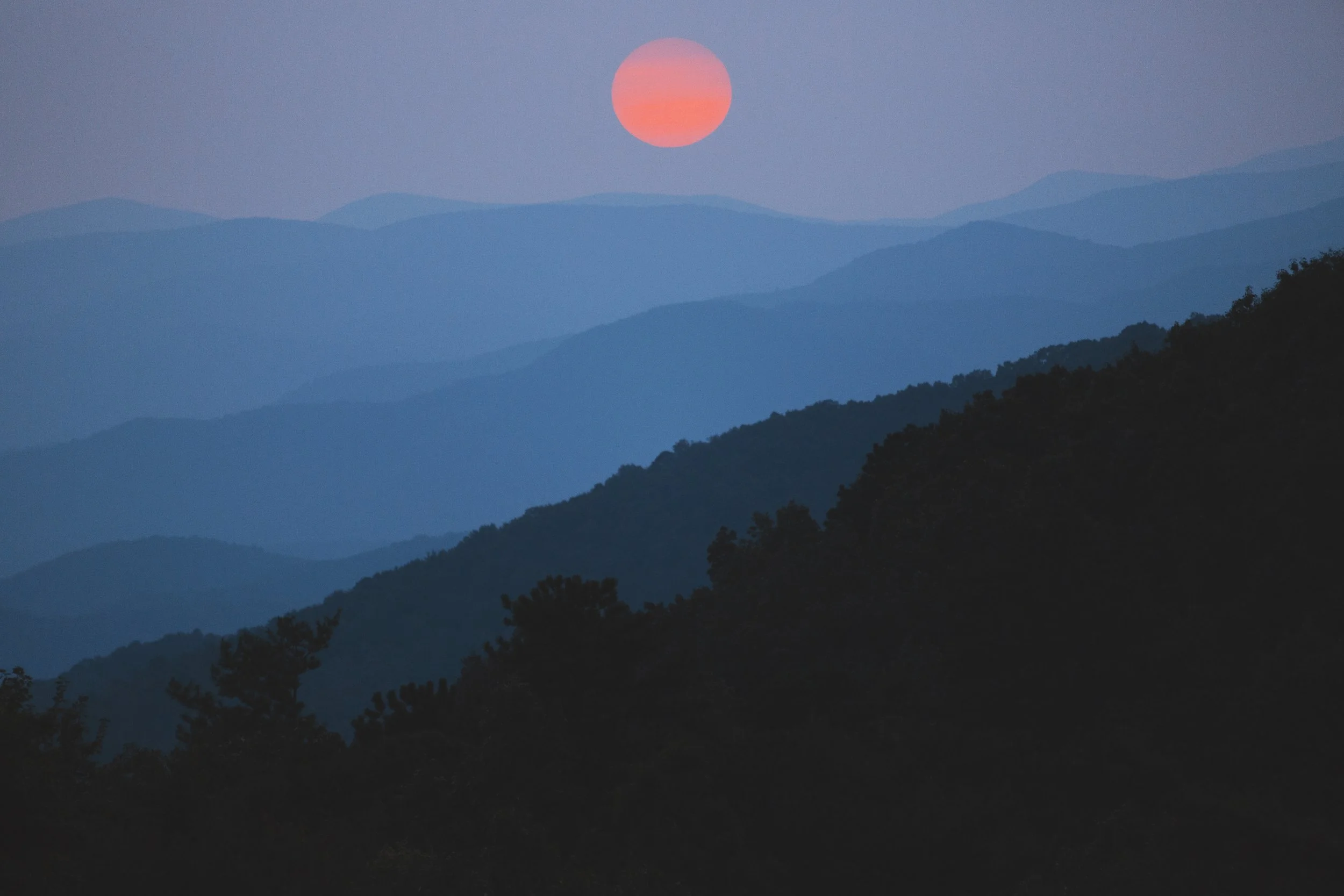 Sunset over layered mountain ranges with a pinkish-orange sun.