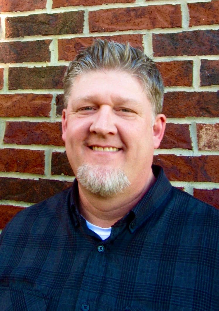 Joseph Davis smiles in front of a brick wall wearing a flannel shirt.