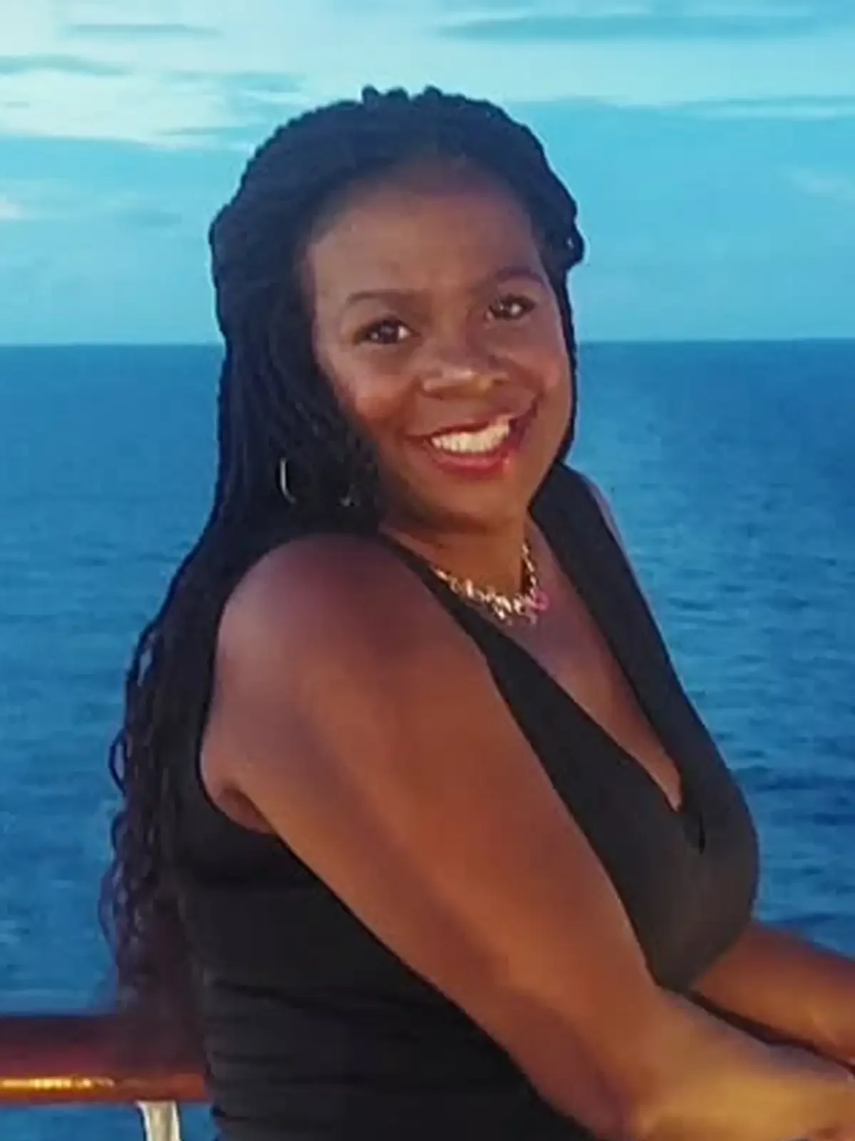 A woman with braided hair smiling on a boat with the ocean in the background.