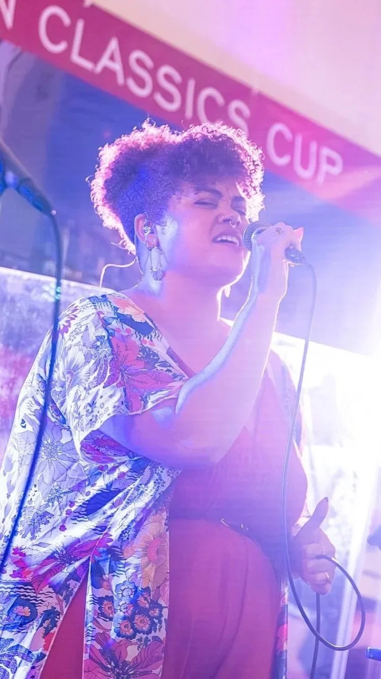 A woman singing into a microphone during a performance, with a sign in the background that reads 'CLASSIC CUP'.