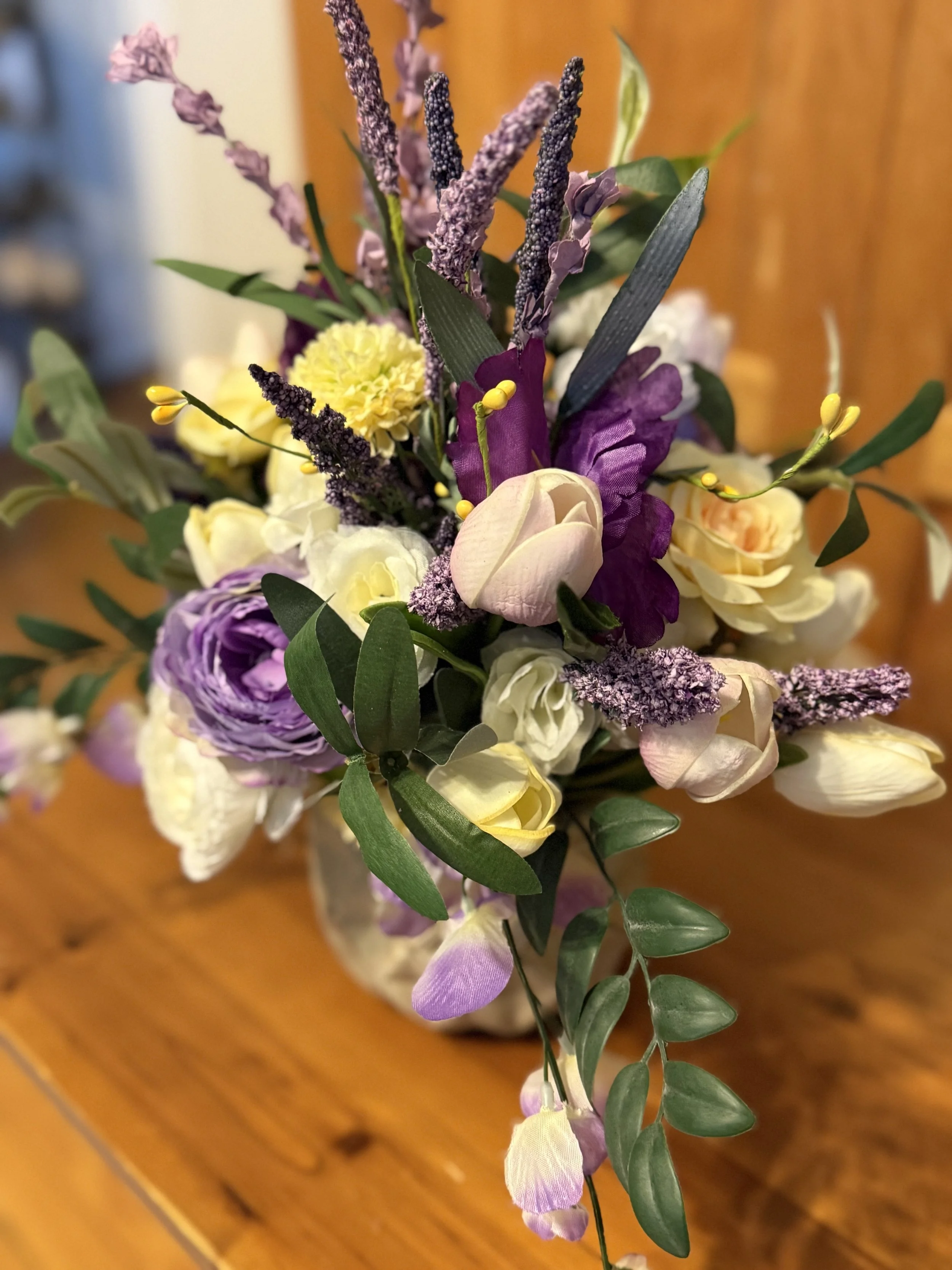 A colorful flower bouquet with purple, yellow, white, and pink flowers on a wooden table.