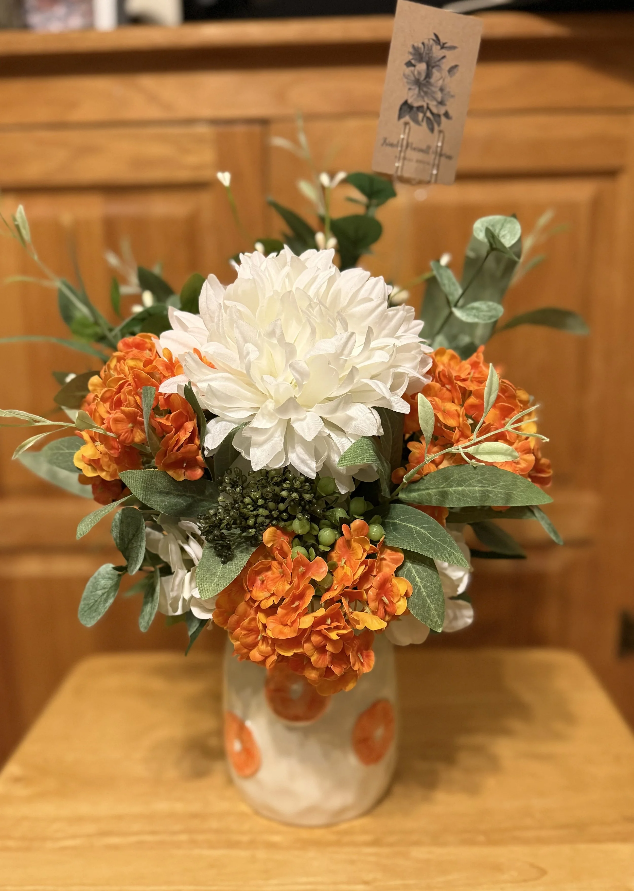A floral arrangement in a white ceramic vase with orange and white flowers, green leaves.