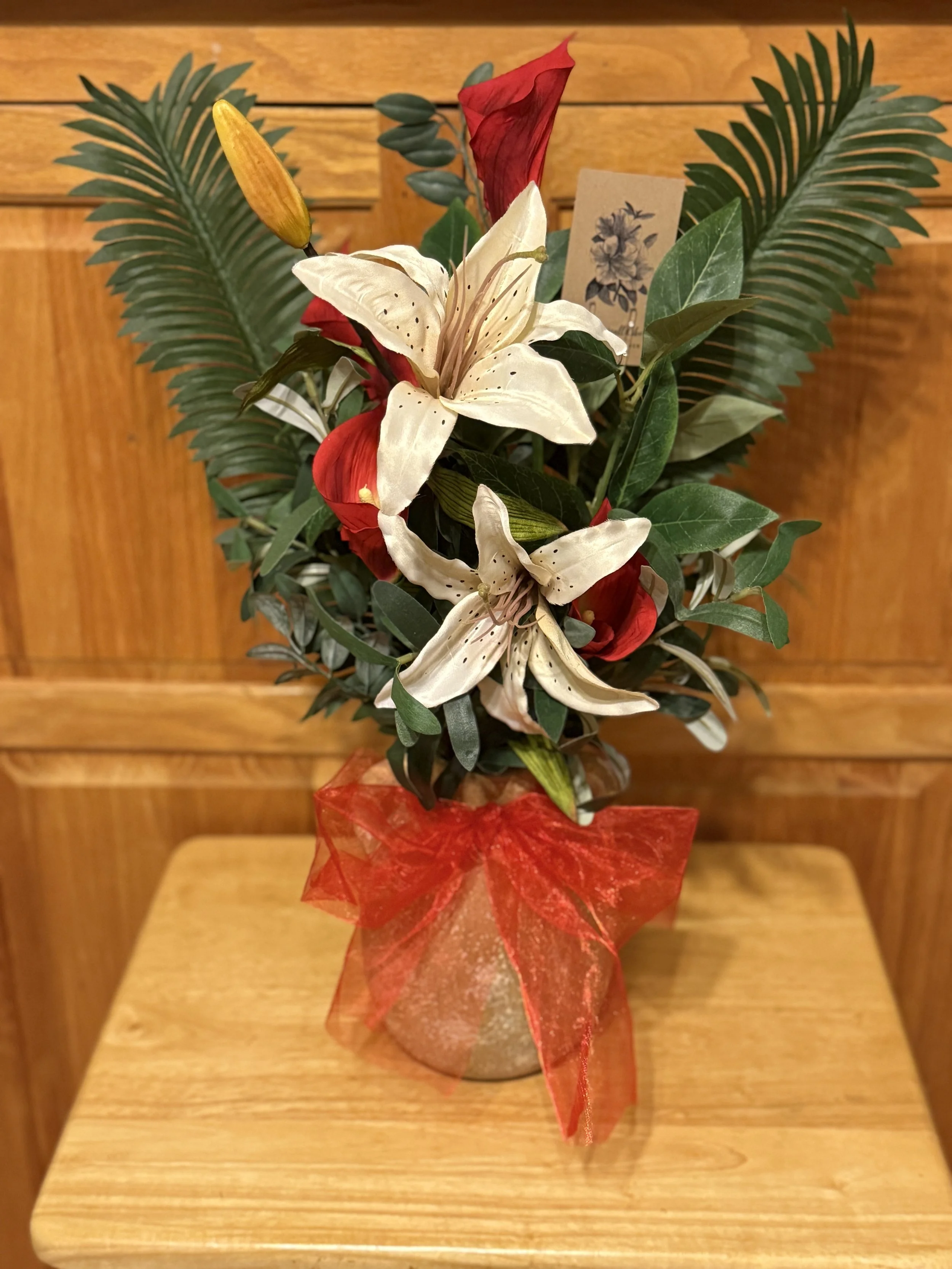 A floral arrangement with lilies, red flowers, and greenery in a wrapped container on a wooden table.