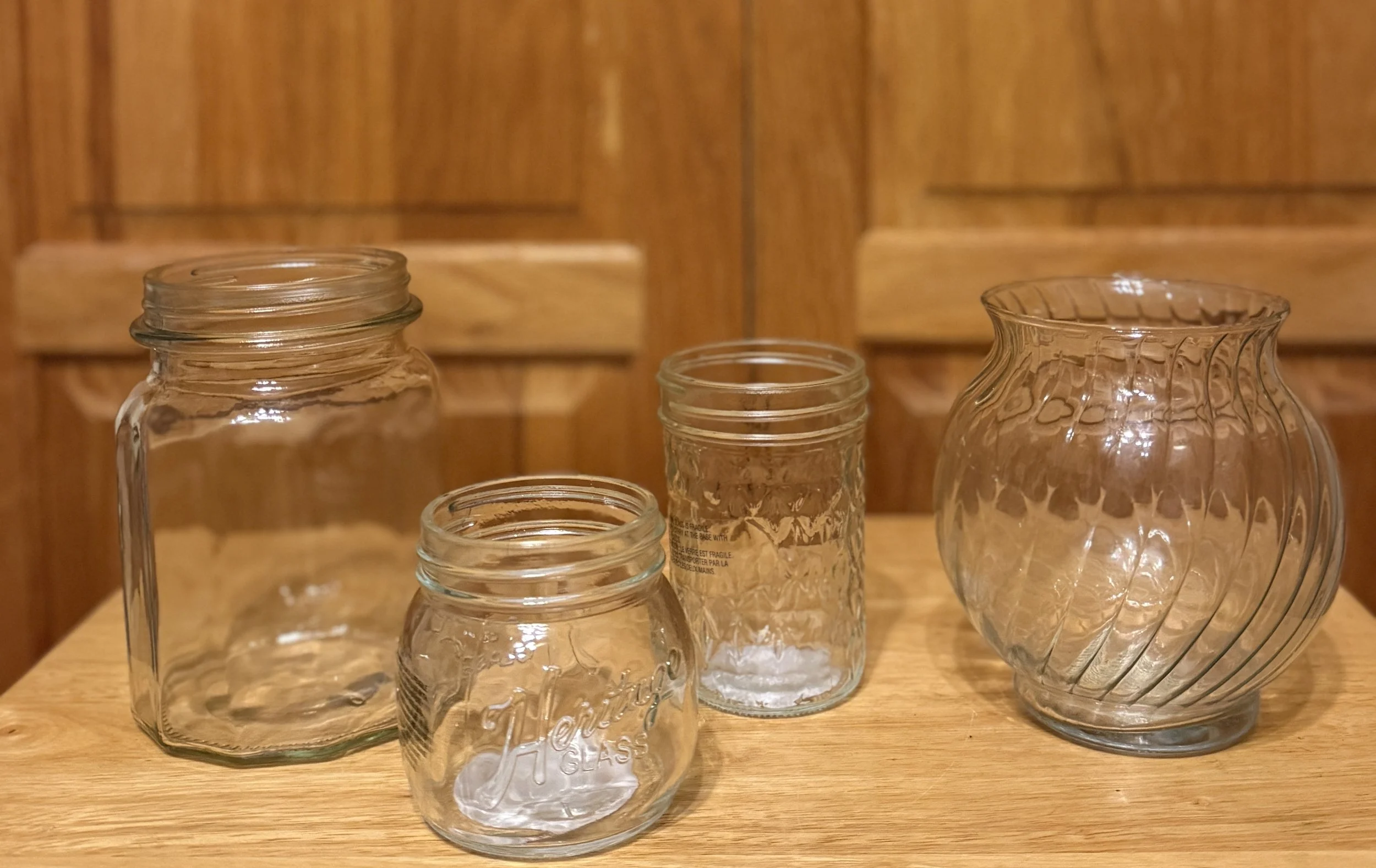 Four empty glass jars of different sizes and shapes on a wooden surface, with a wooden background.