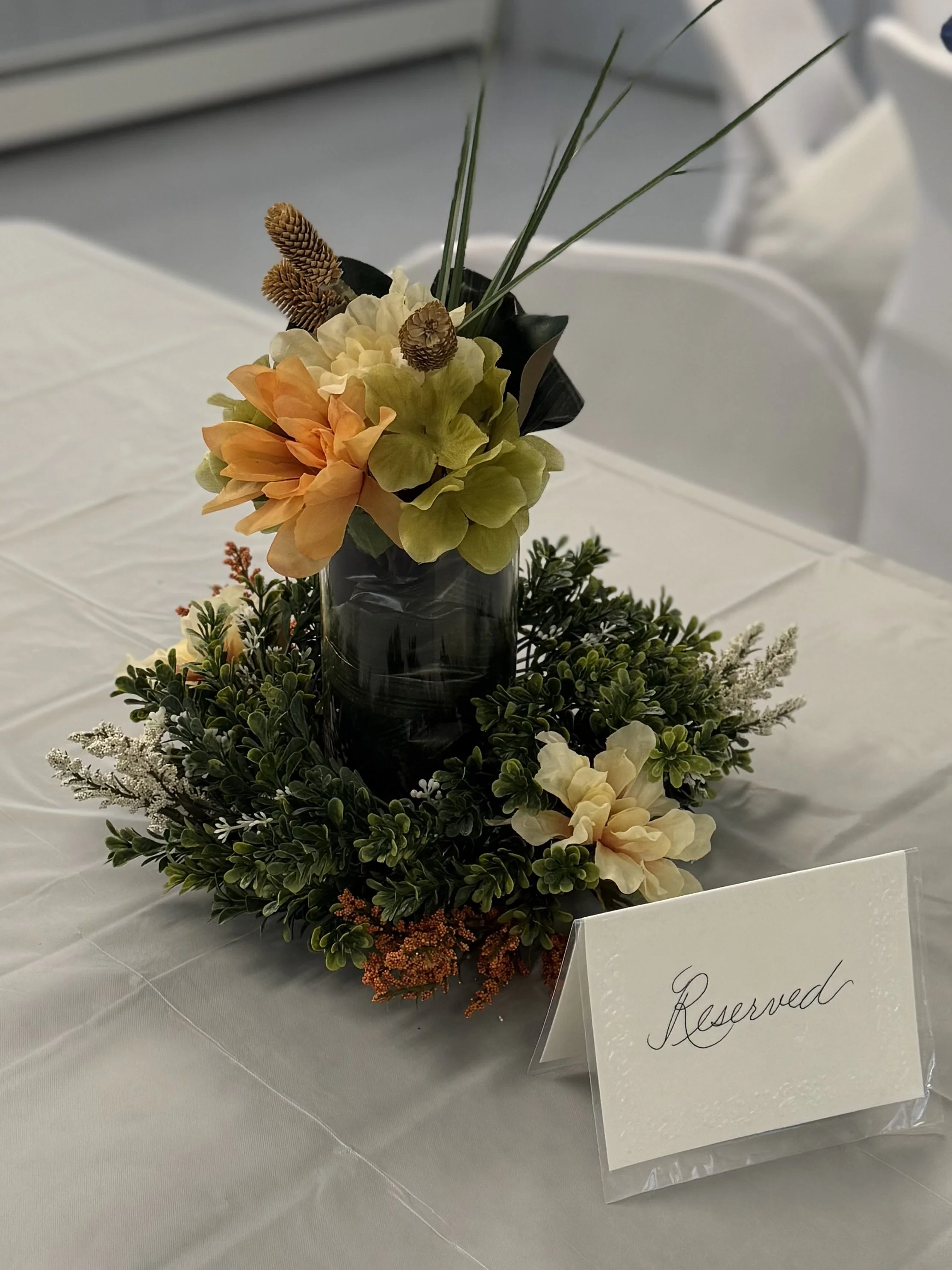 Flower arrangement with orange and cream flowers in a black vase on a table with a reserved sign in front.