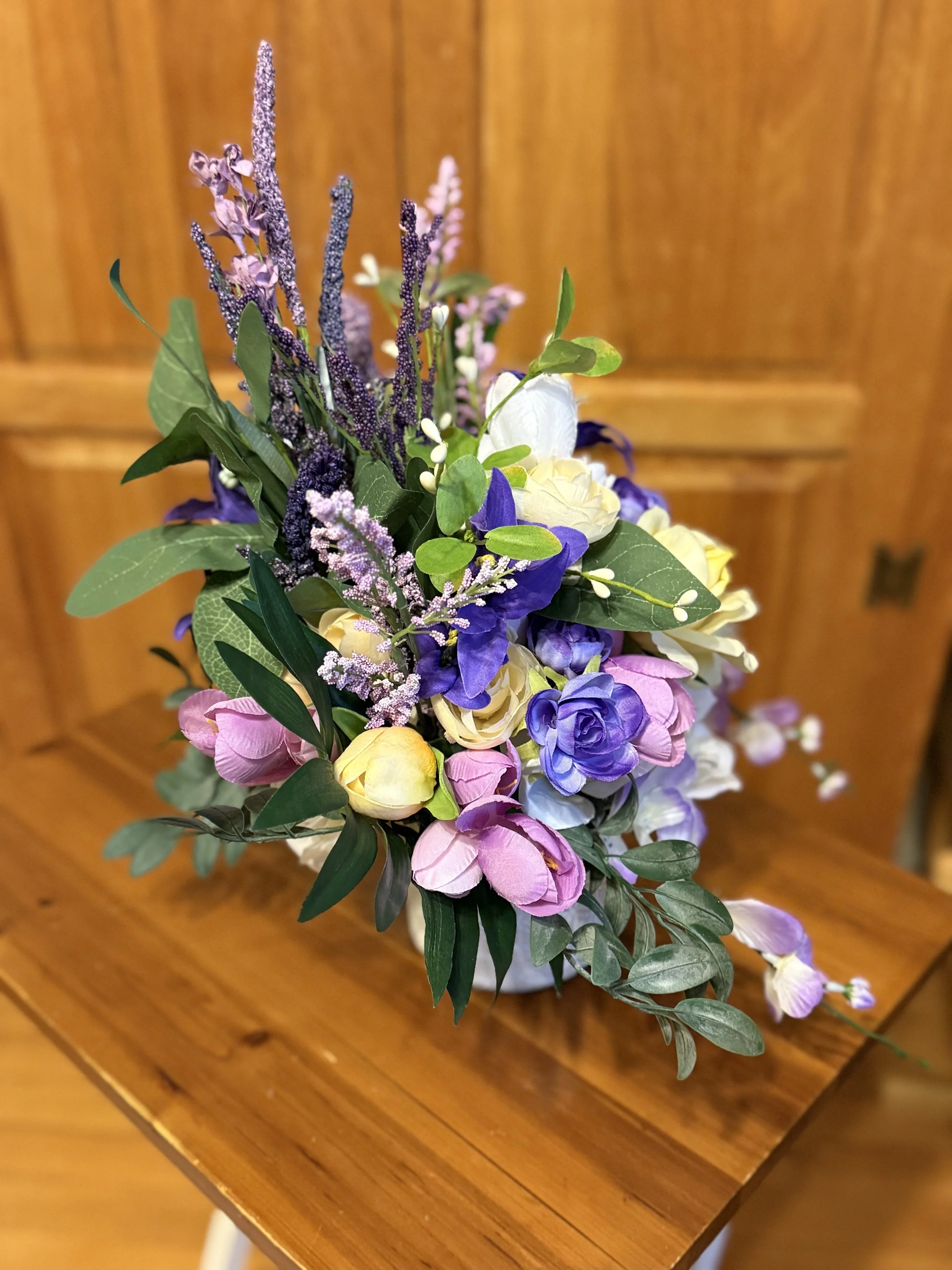 Colorful bouquet of flowers including purple, pink, white, and yellow blooms on a wooden surface with a wooden background.
