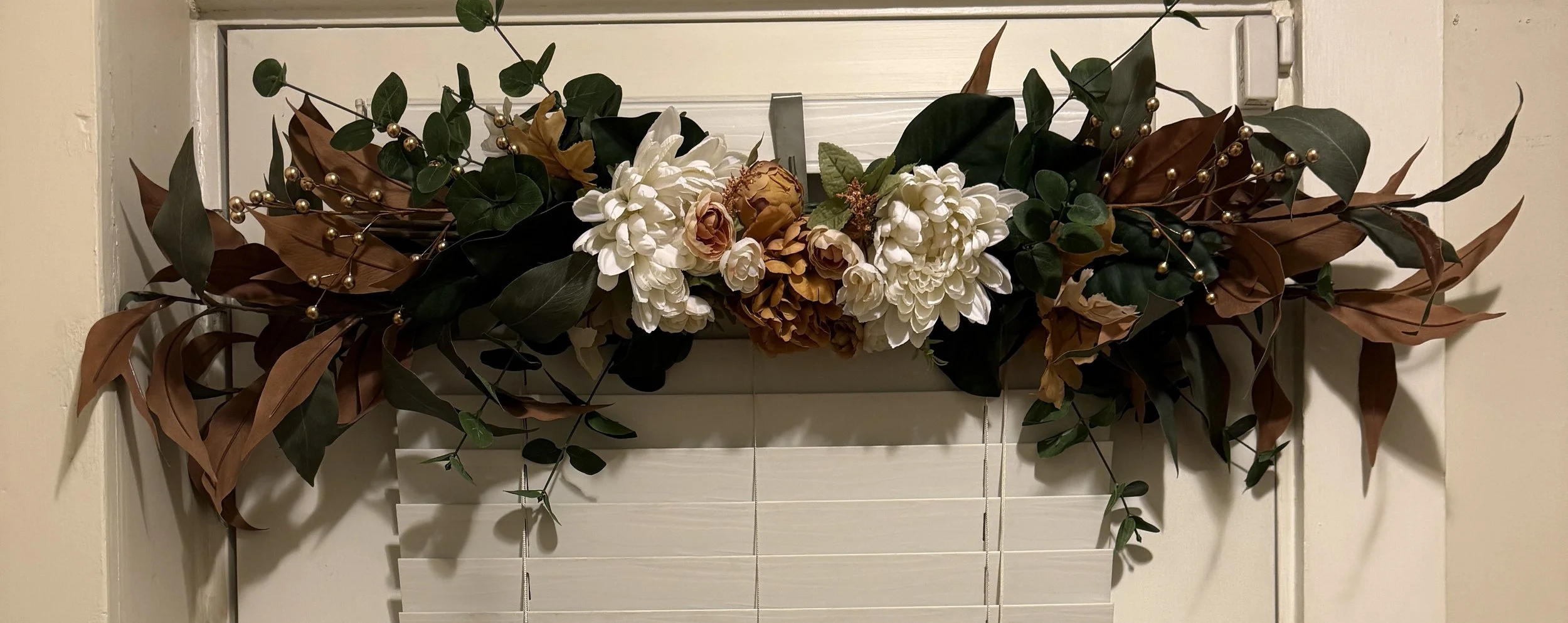 Fall floral swag with white, beige, and brown flowers, green and brown leaves, and gold decorative beads.
