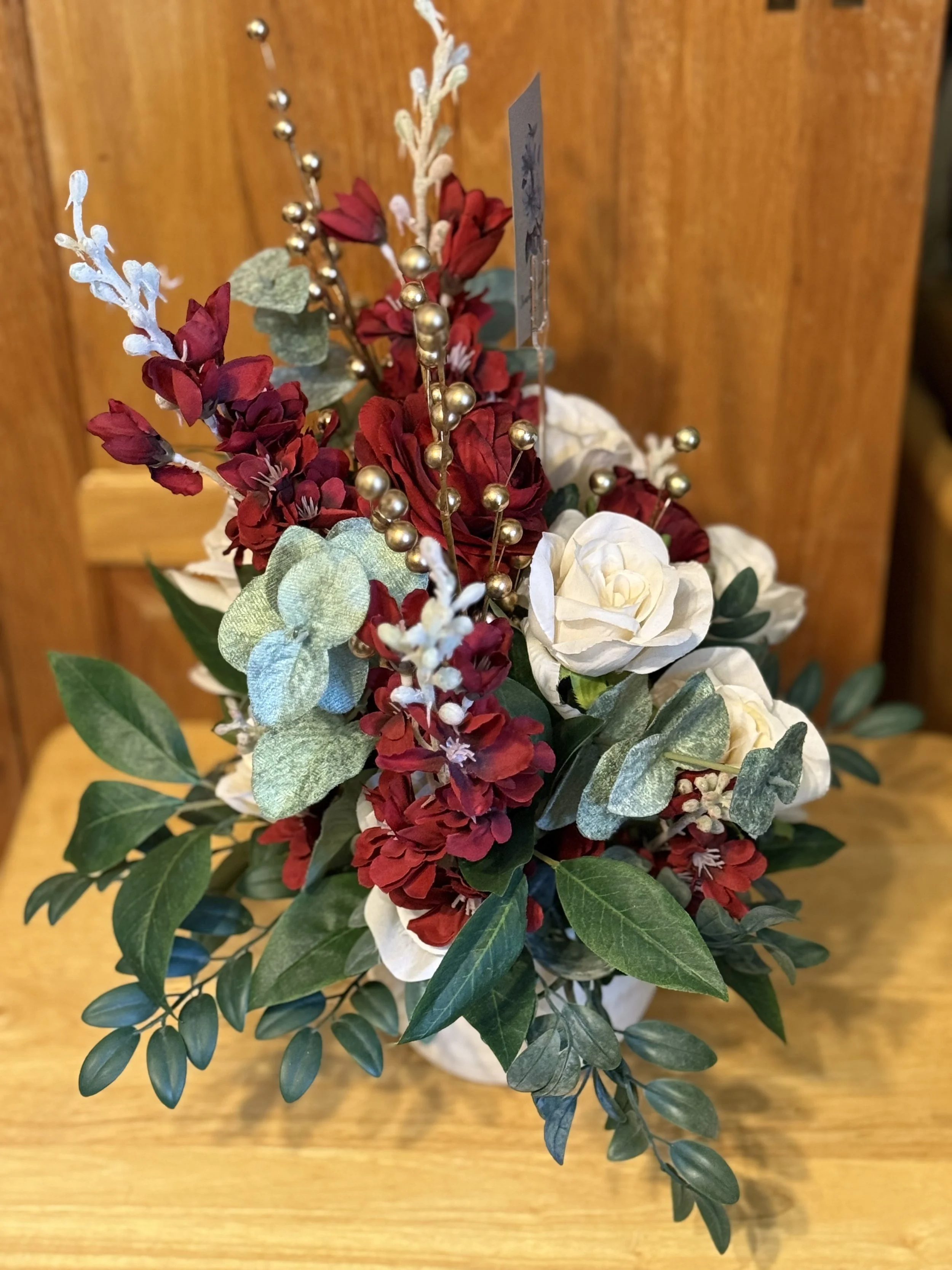 A festive floral arrangement with red, white, and green artificial flowers and leaves, accented with gold and silver decorative beads.