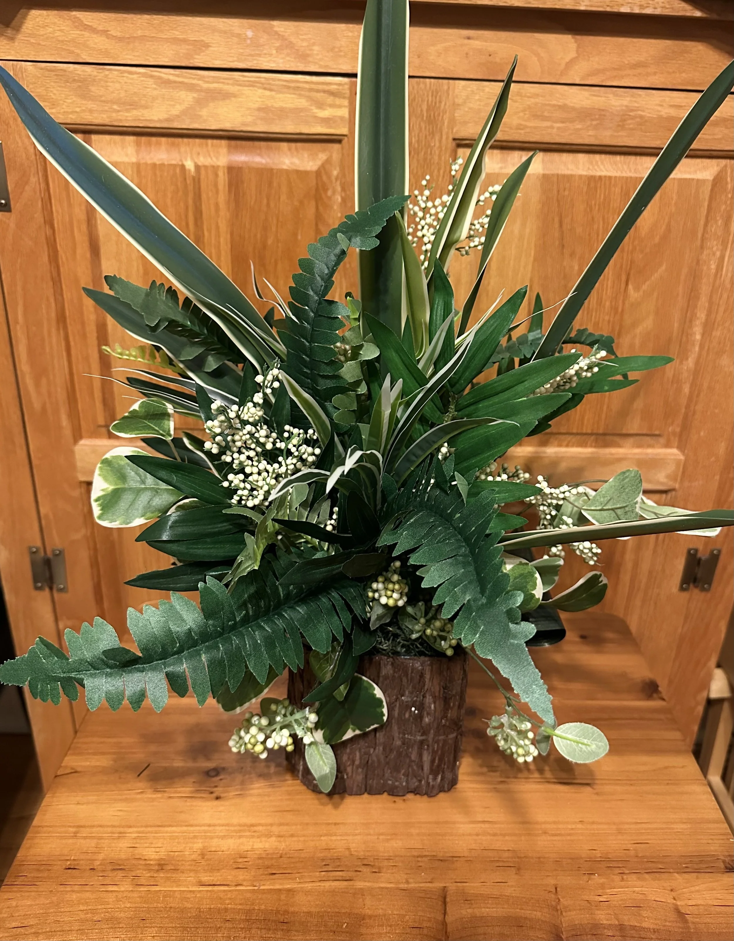 A floral arrangement with green leaves and white flowers in a tree bark vase.