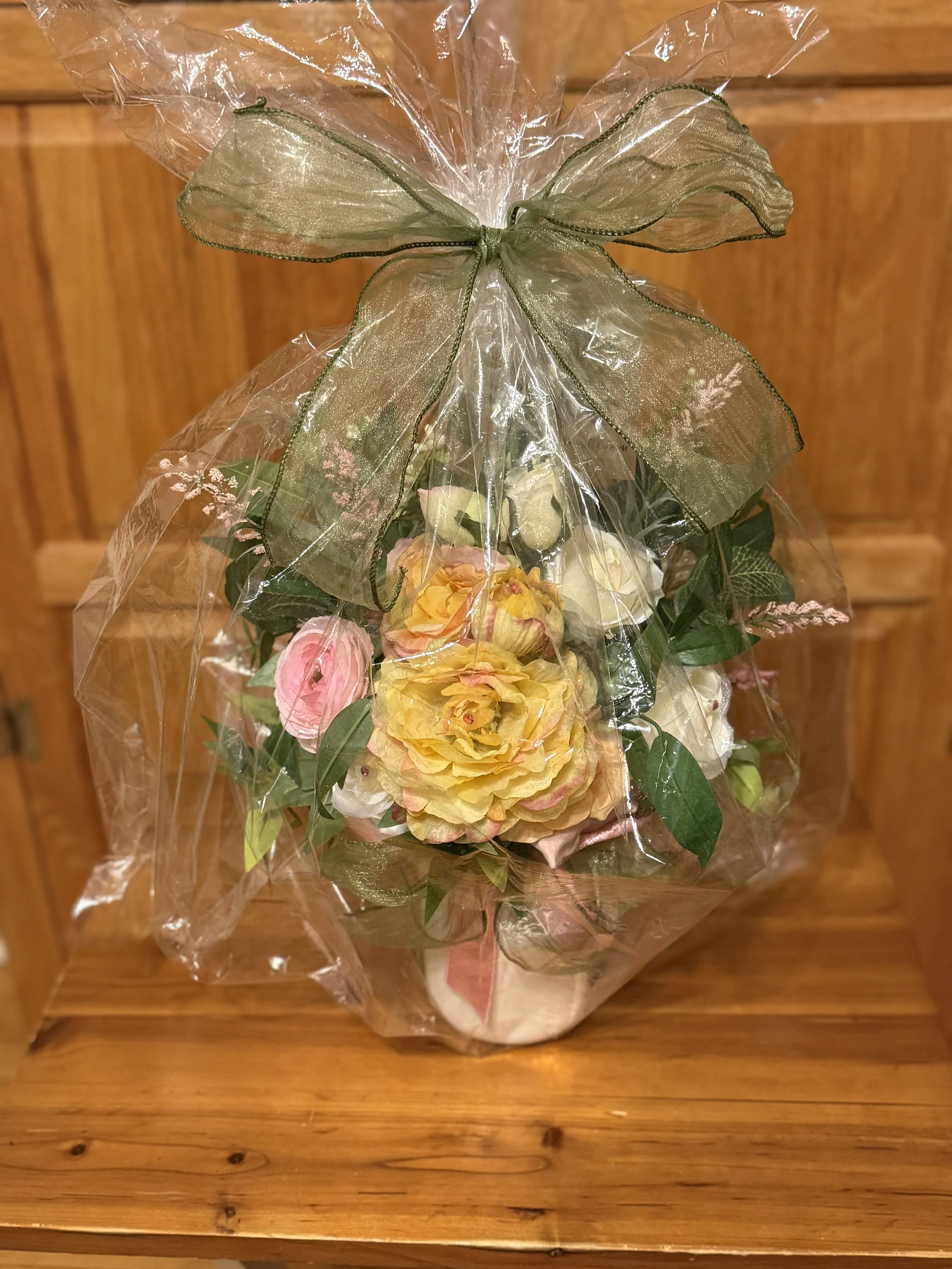 A bouquet of mixed flowers wrapped in clear plastic with a green ribbon, placed on a wooden surface.