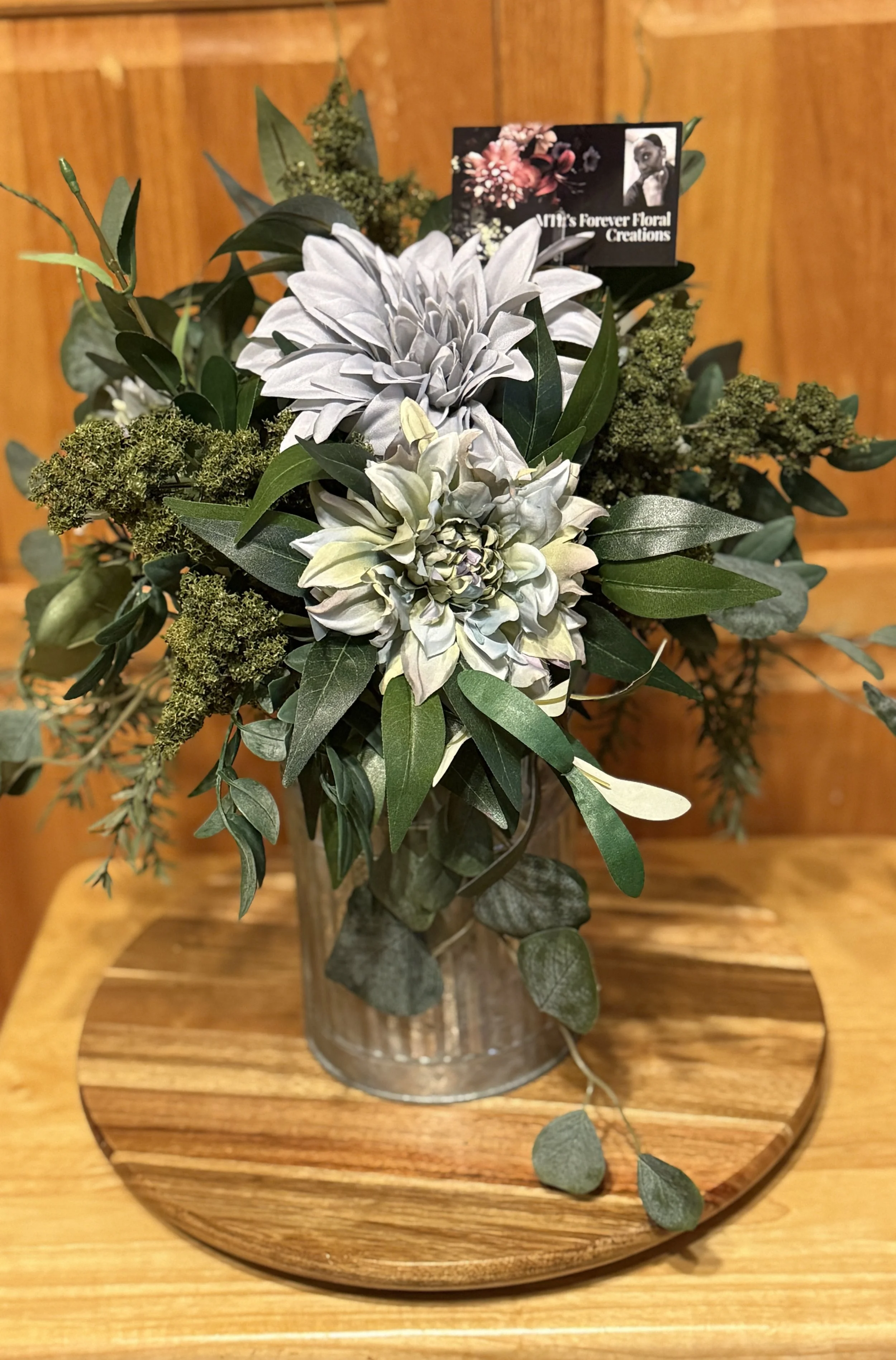 A floral arrangement with white, and gray flowers completed with greenery fillers into a gray tin vase.