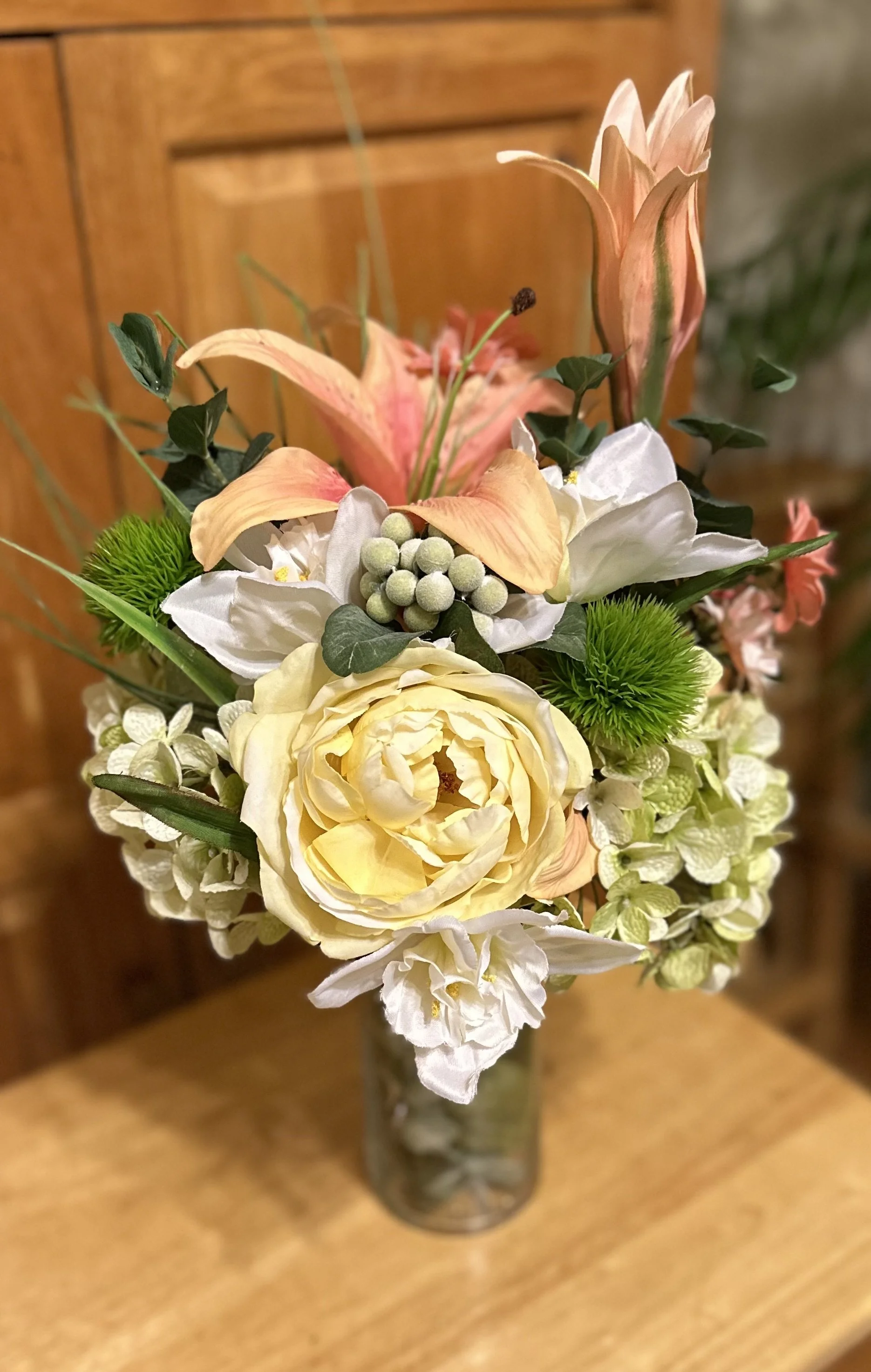 A colorful artificial flower bouquet in a glass vase on a wooden table.