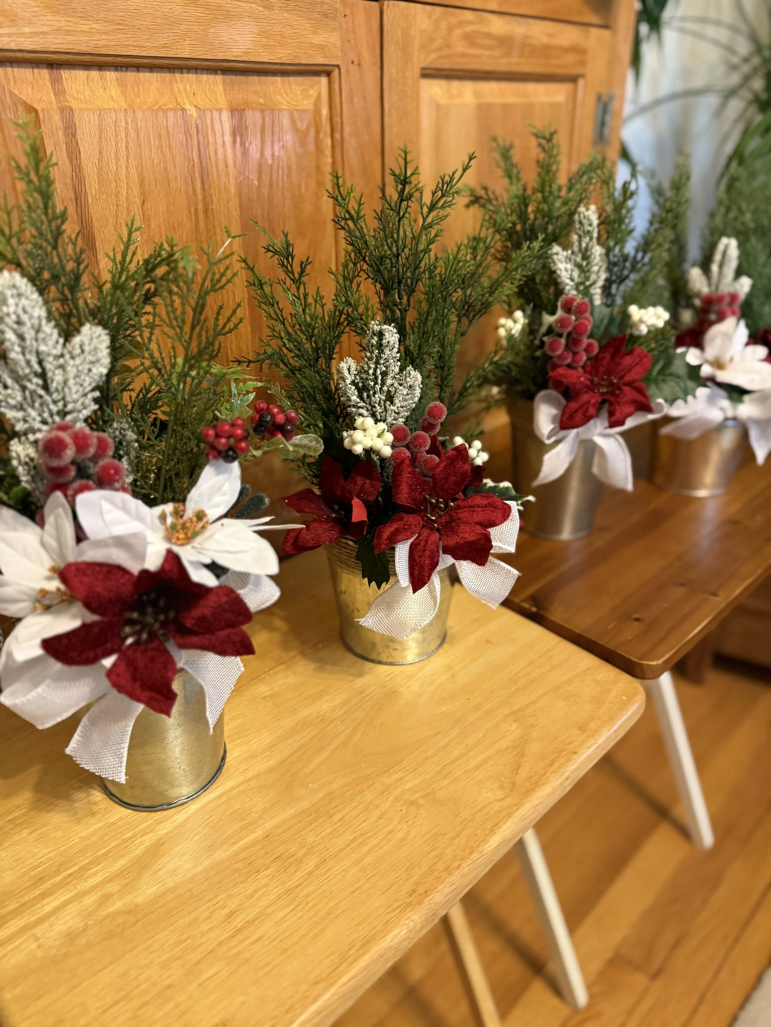 Decorative holiday floral arrangements with poinsettias, evergreen branches, berries in silver tin pots.