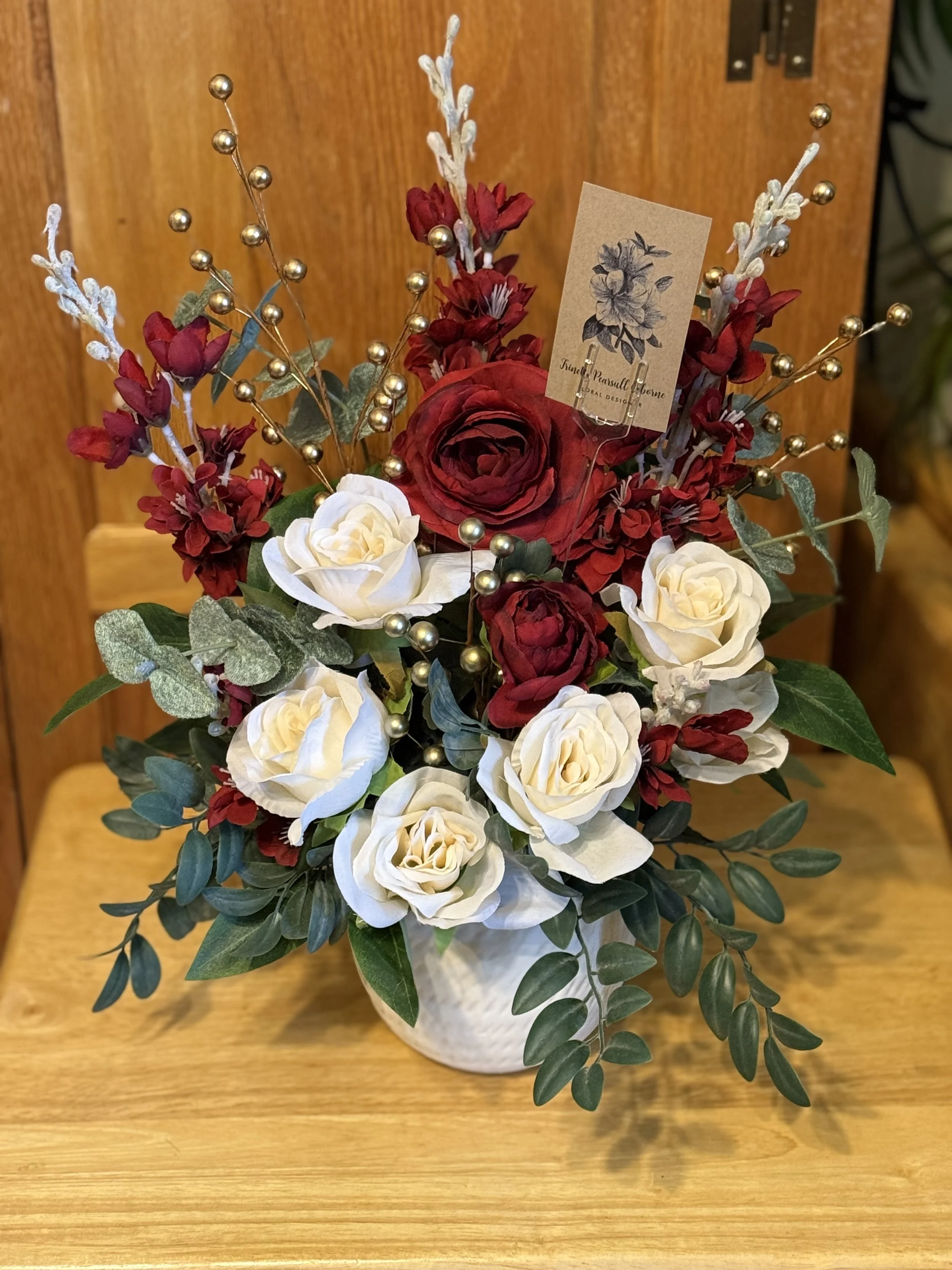 A floral arrangement in a white ceramic vase featuring red and white roses flowers, and decorative gold berries.