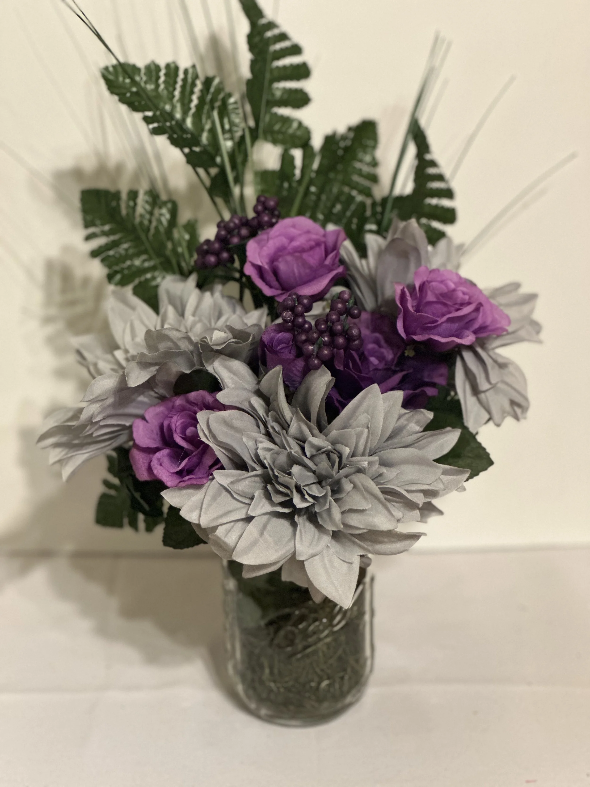 Artificial flower bouquet with purple and white flowers and green foliage in a glass jar.