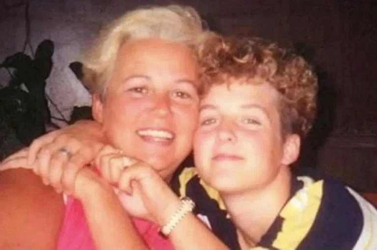 A woman with short blond hair and a young boy with curly hair, both smiling and hugging each other closely.