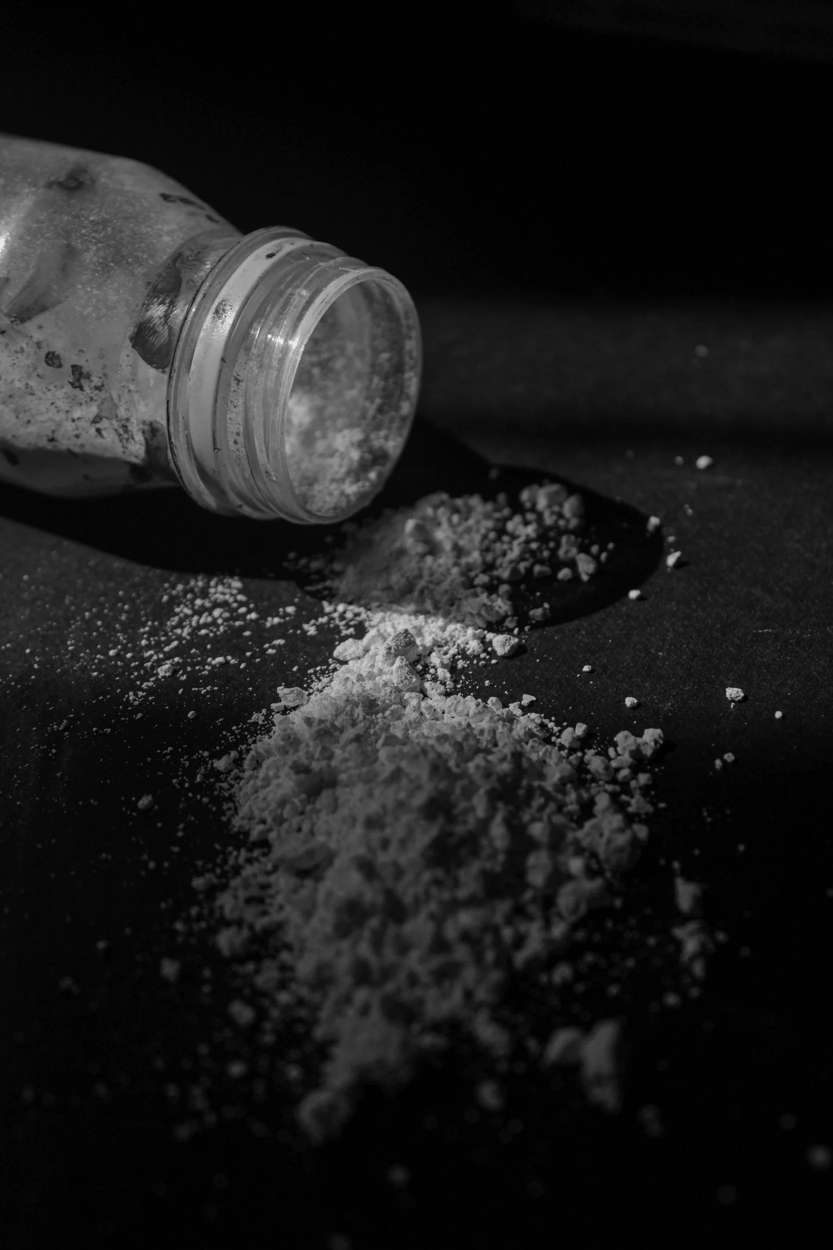 A glass jar tipped over with white powder spilled on a dark surface