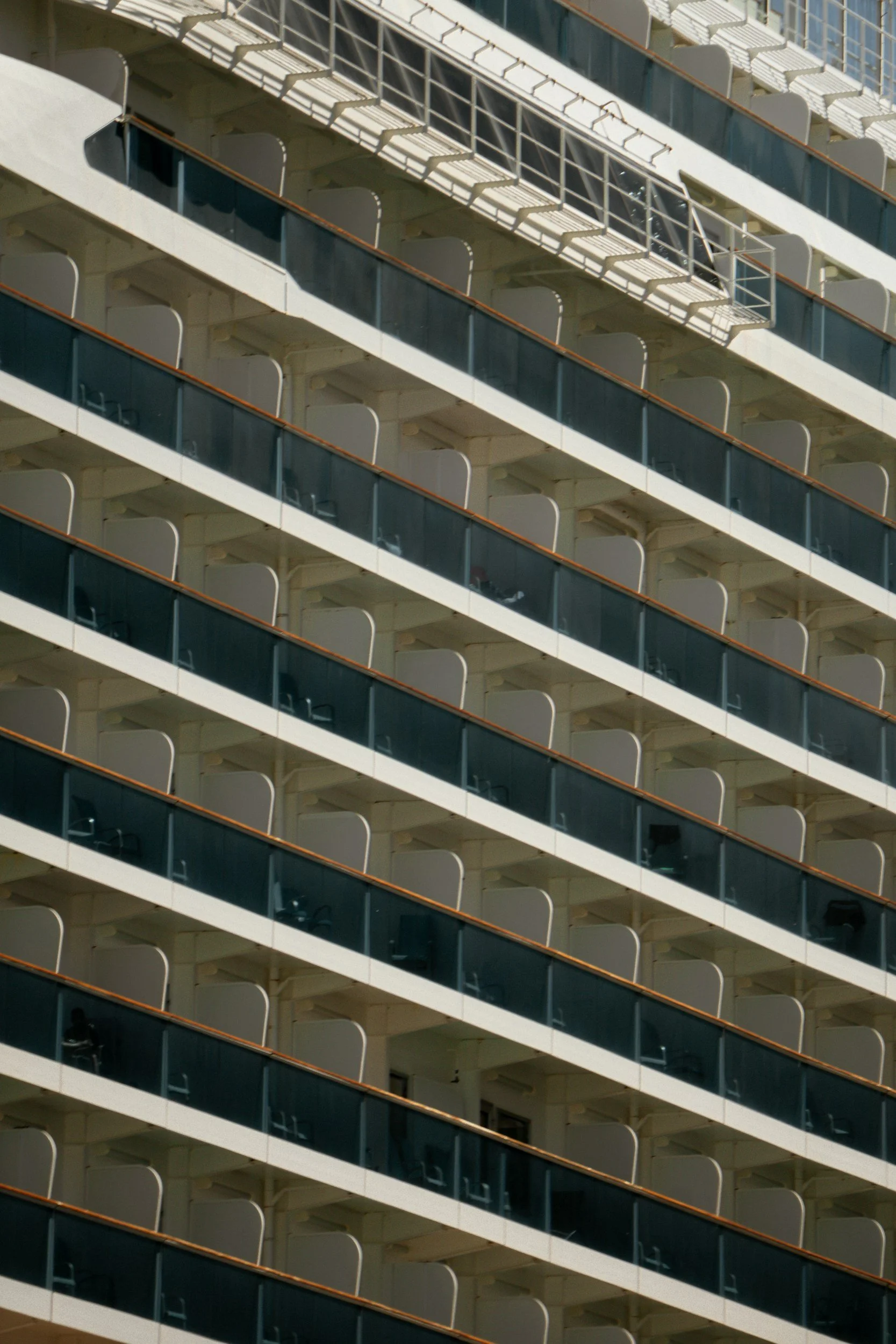 Close-up view of the balconies on a cruise ship or tall building, showing multiple levels with glass railings and chairs visible on some balconies.