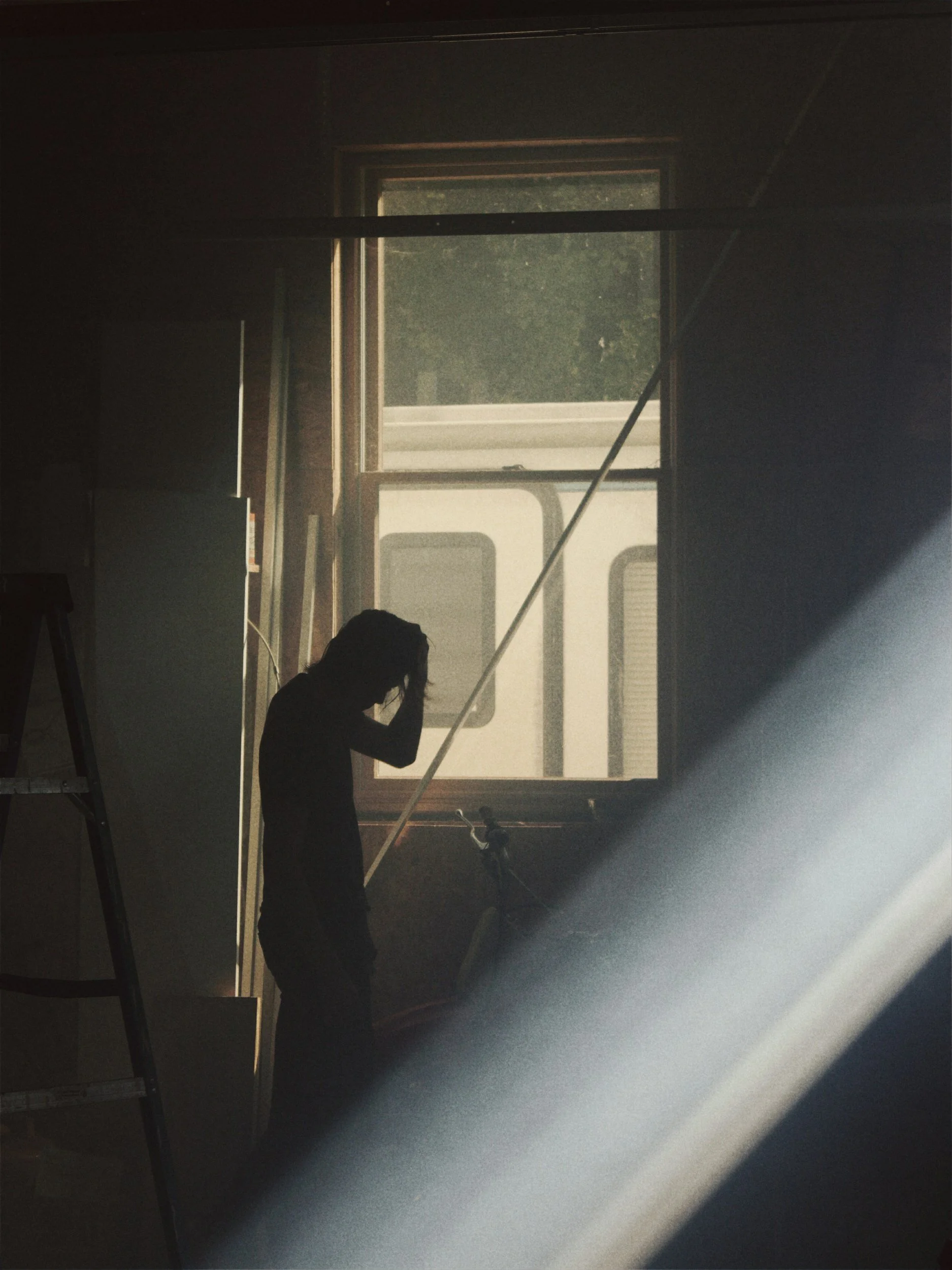 Person sitting on snow-covered ledge looking out at the ocean through an open window with cloudy sky