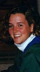 Person sitting on snow-covered ledge looking out at the ocean through an open window with cloudy sky