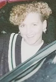 Person sitting on snow-covered ledge looking out at the ocean through an open window with cloudy sky