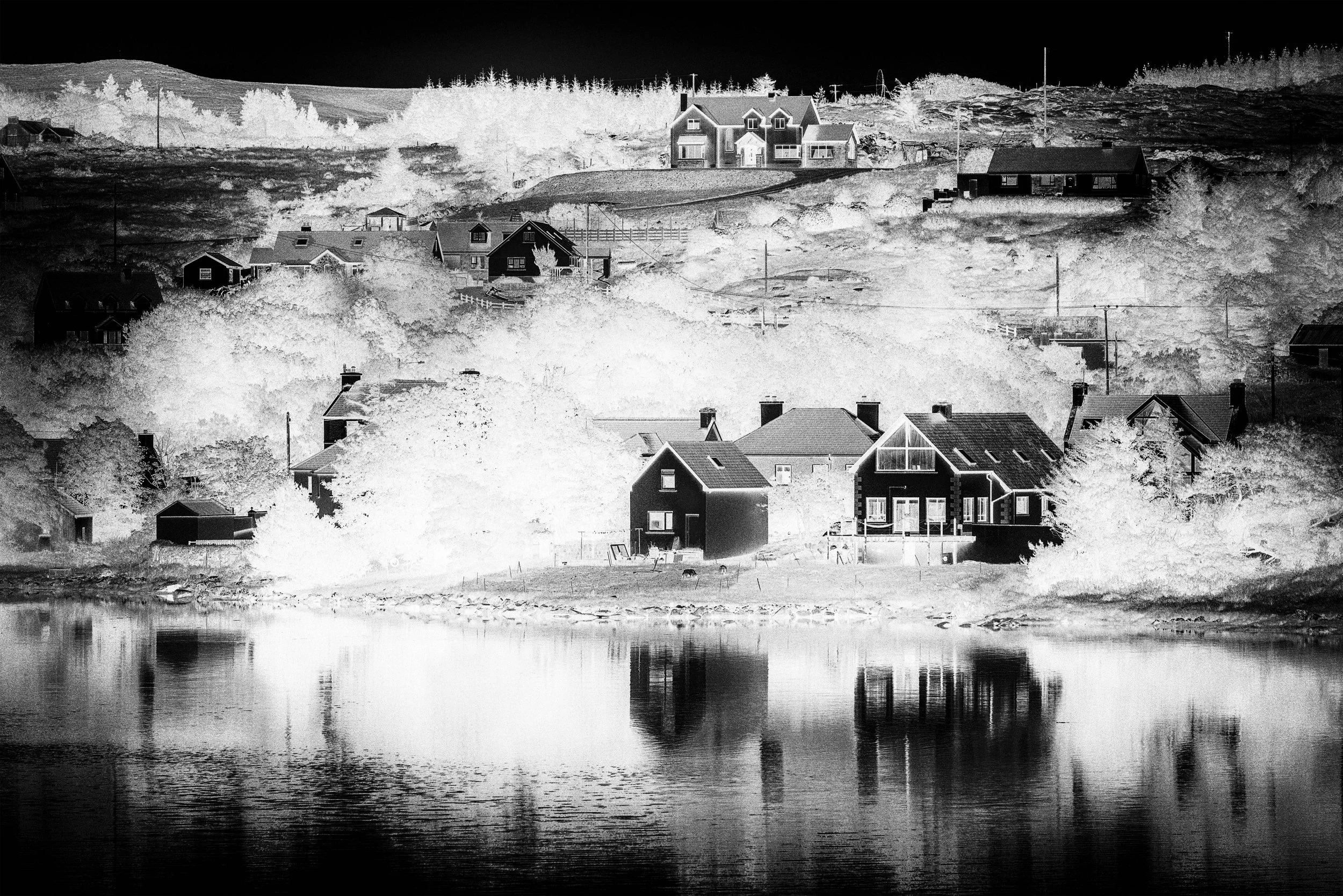 black and white negative landscape image of a quiet seaside harbour of small cottages with the hillside behind