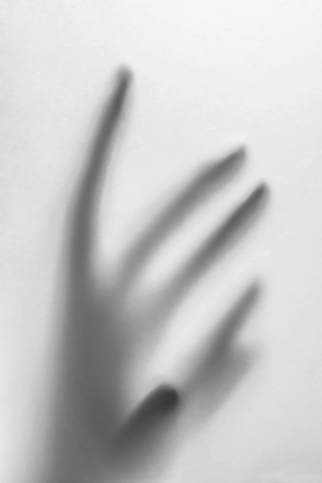 A blurred black-and-white image of a hand with fingers slightly spread apart against a plain background.