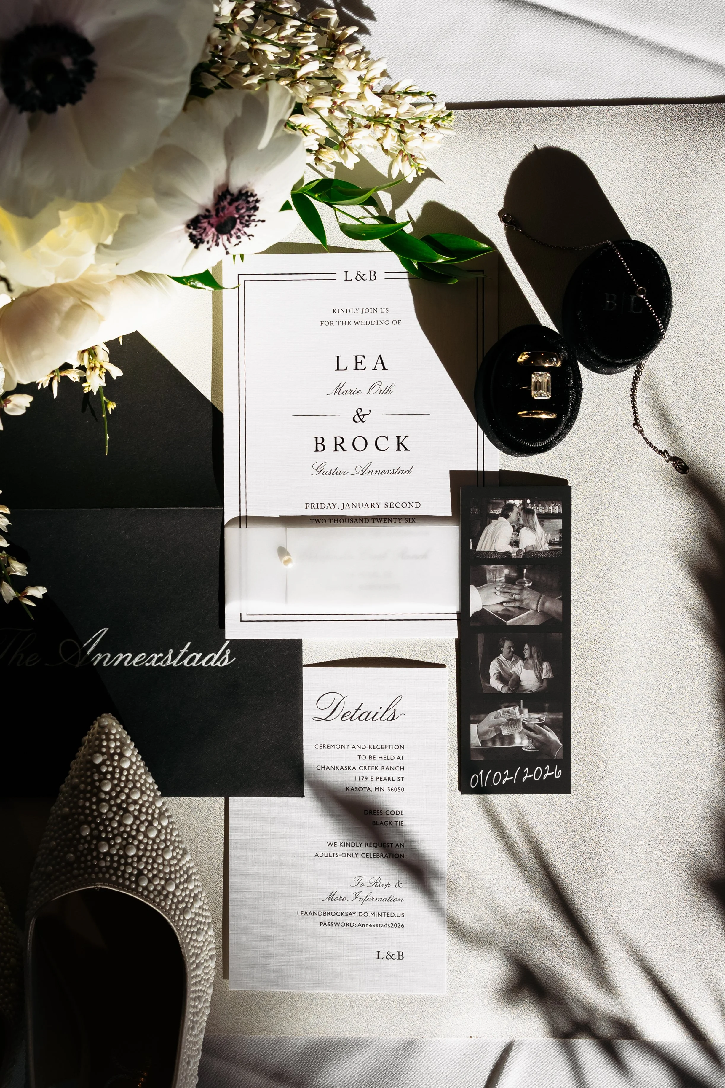 Wedding invitation suite with floral accents, jewelry, photo booth strip, and a white high heel shoe decorated with pearls.