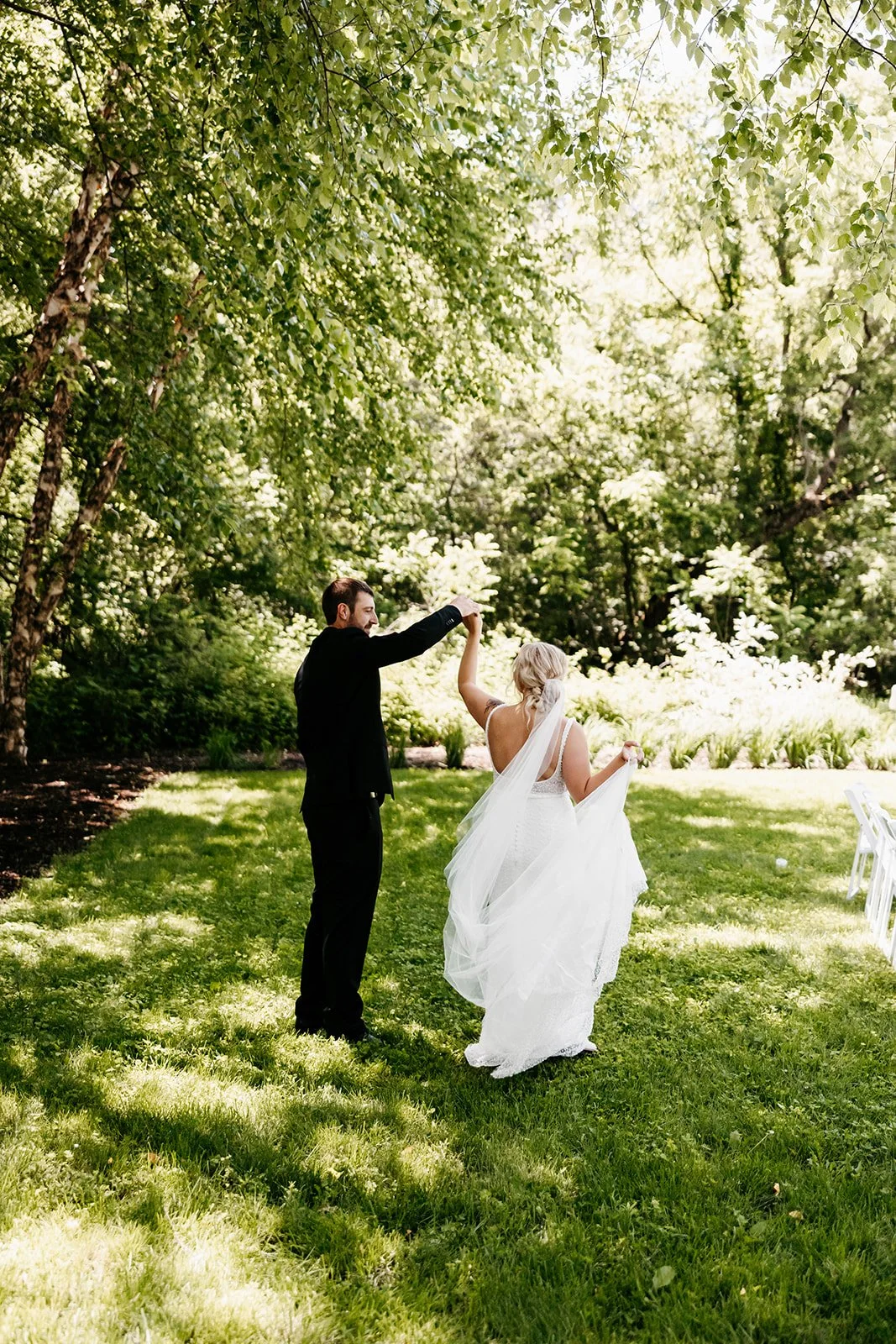 Bride and groom dancing outdoors on a grassy area under leafy trees